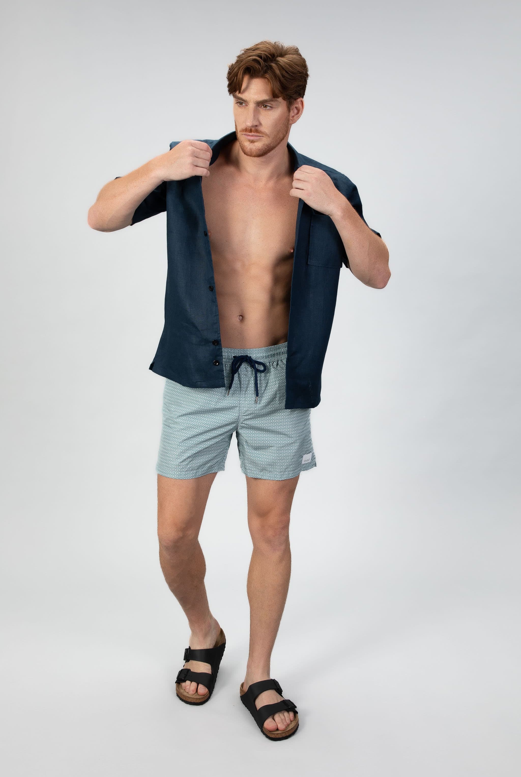 Arrow patterned swim shorts in Aqua turquoise with a navy shirt on a light gray background