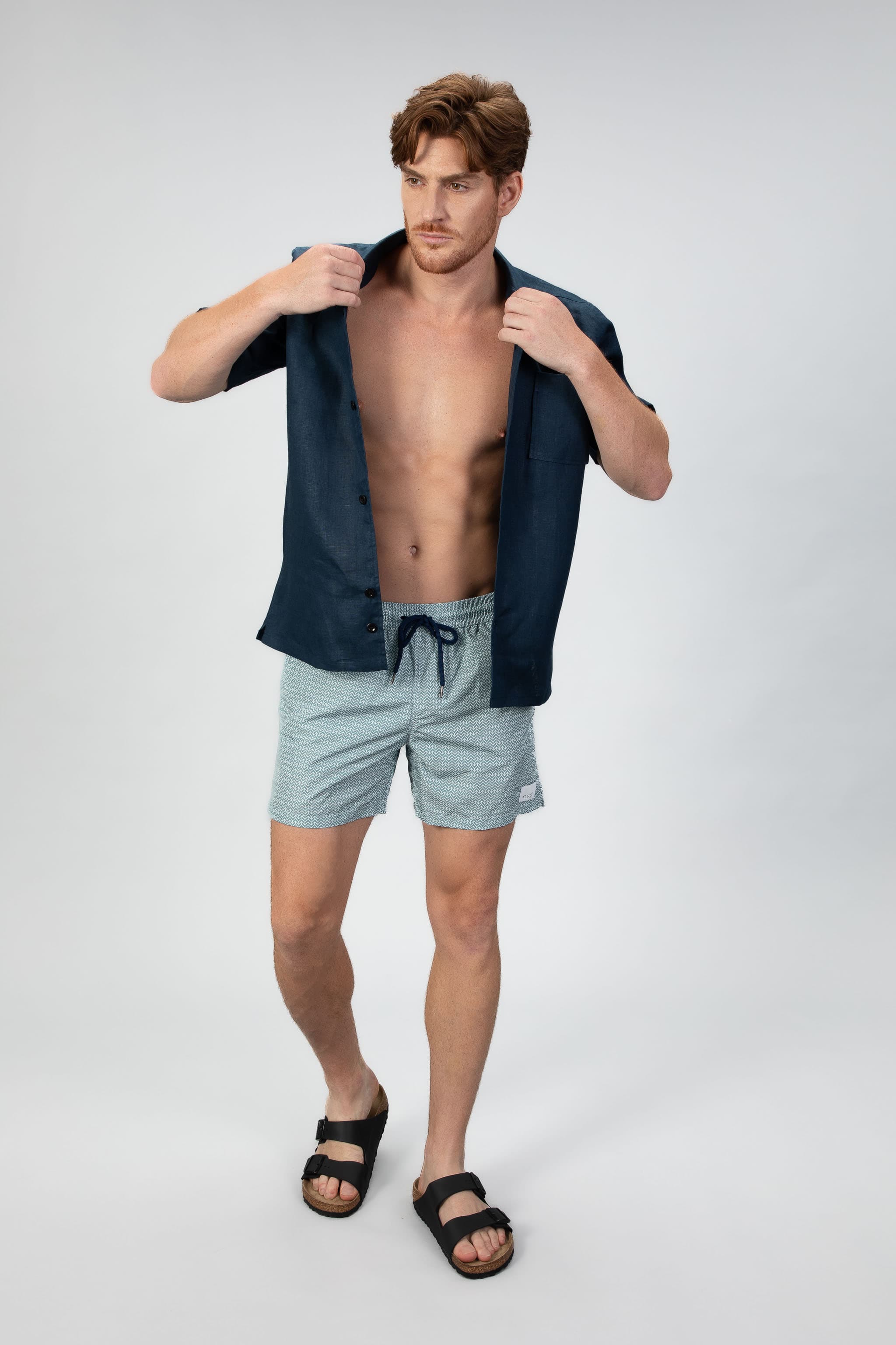 Arrow patterned swim shorts in Aqua turquoise with a navy shirt on a light gray background