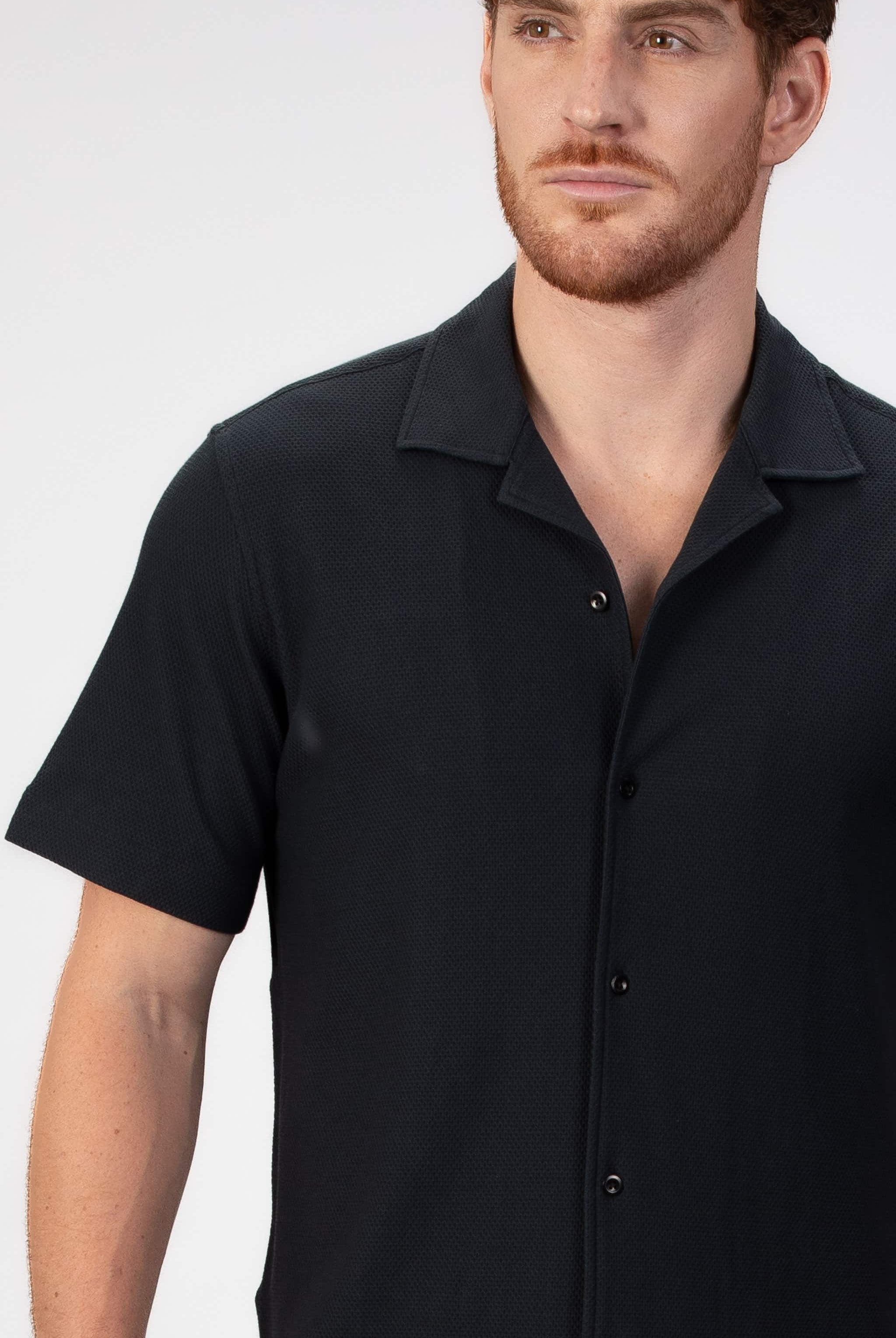 Man wearing a black short-sleeve camp collar shirt on a plain background