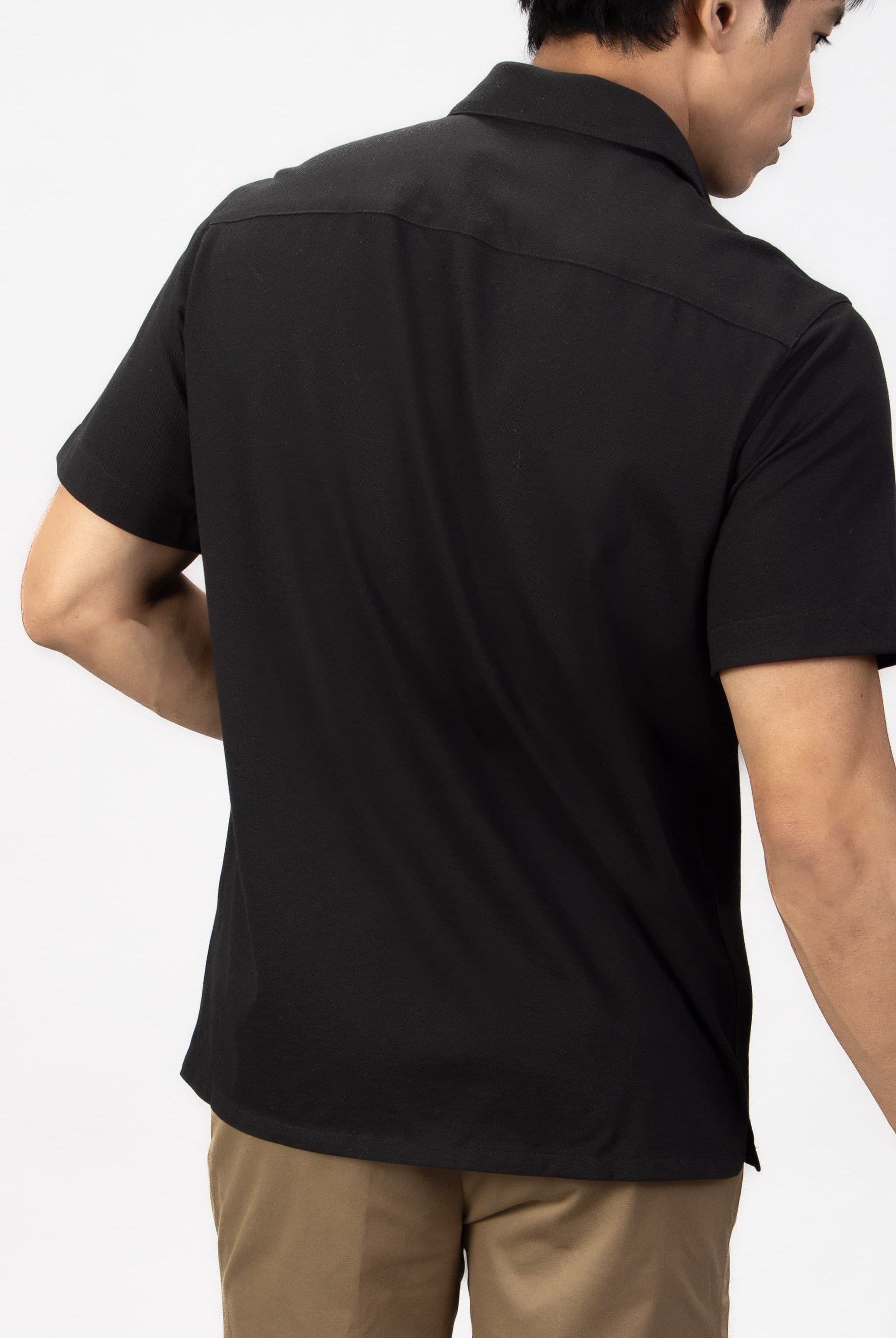 Man wearing a black piquet short sleeve shirt with beige cotton stretch shorts.