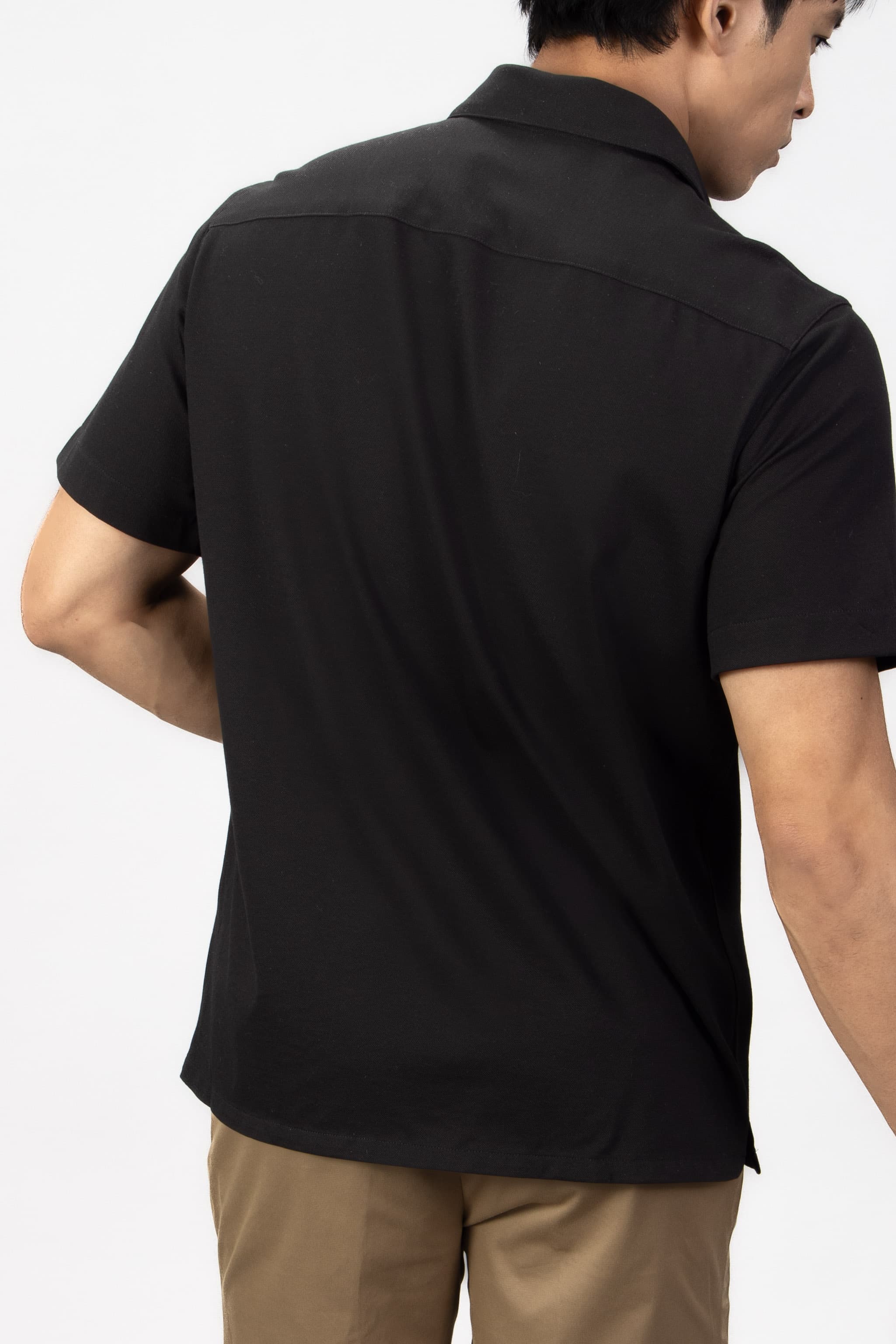 Man wearing a black piquet short sleeve shirt with beige cotton stretch shorts.