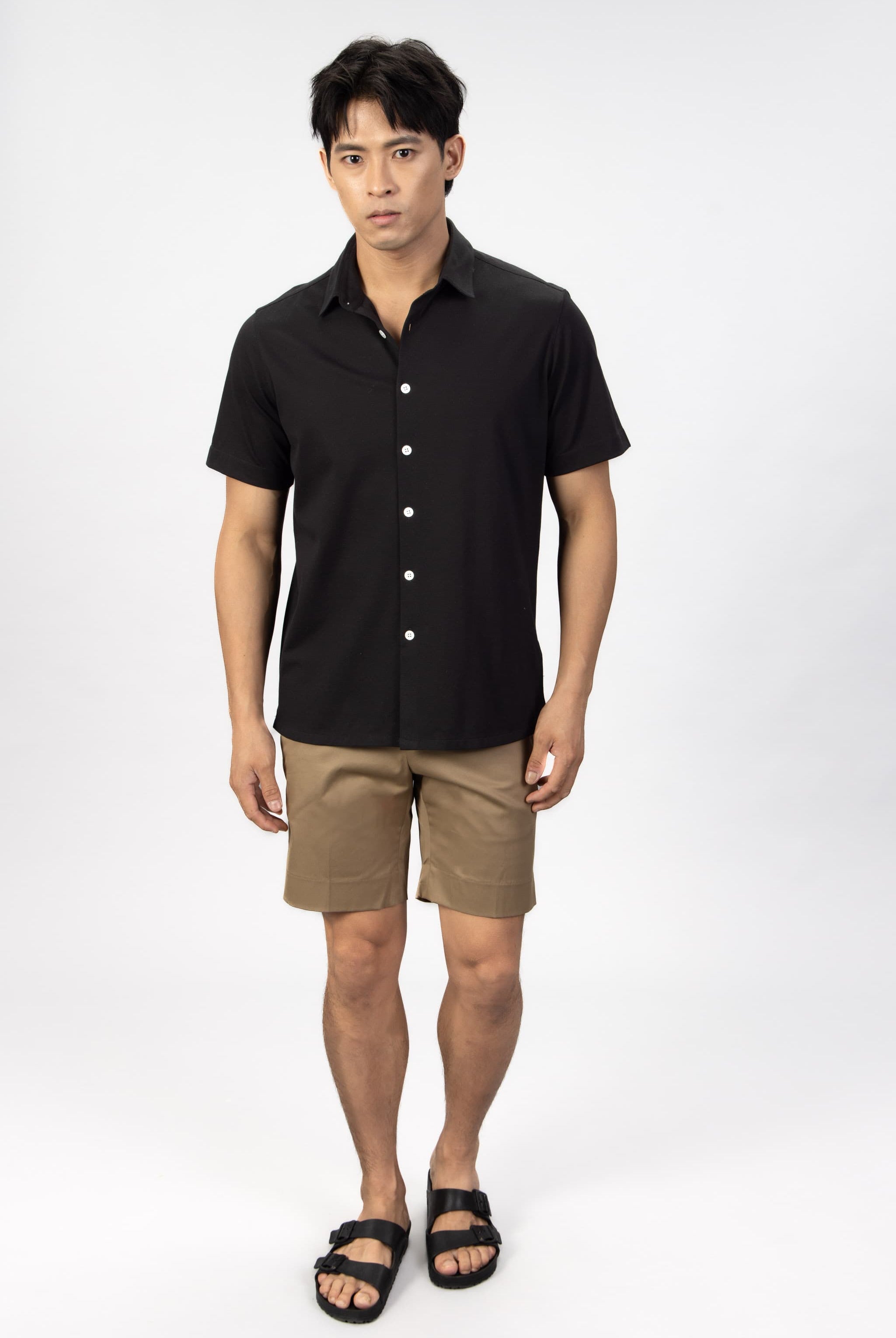 Man wearing a black piquet short sleeve shirt with beige cotton stretch shorts.
