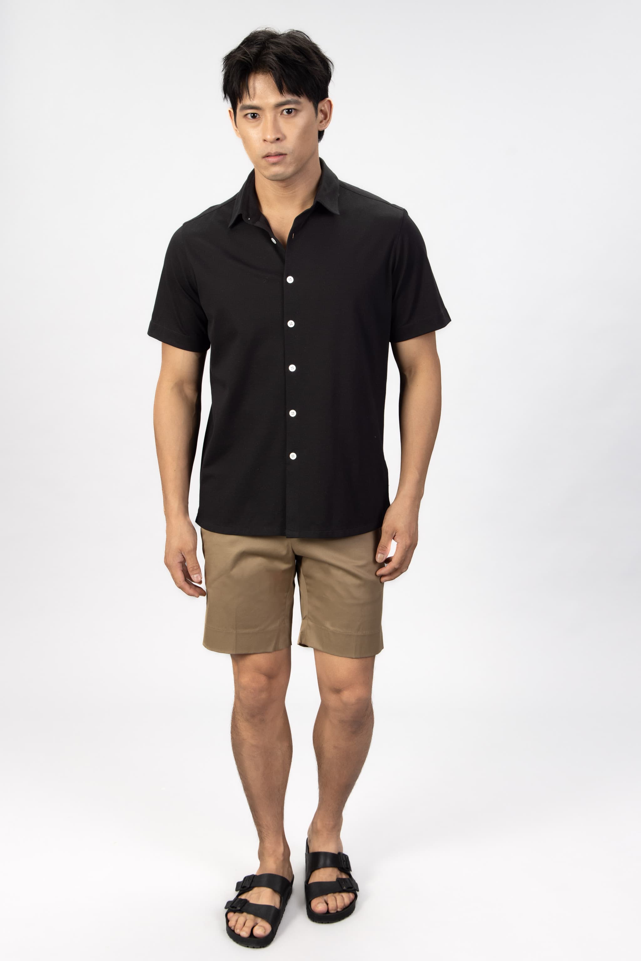 Man wearing a black piquet short sleeve shirt with beige cotton stretch shorts.