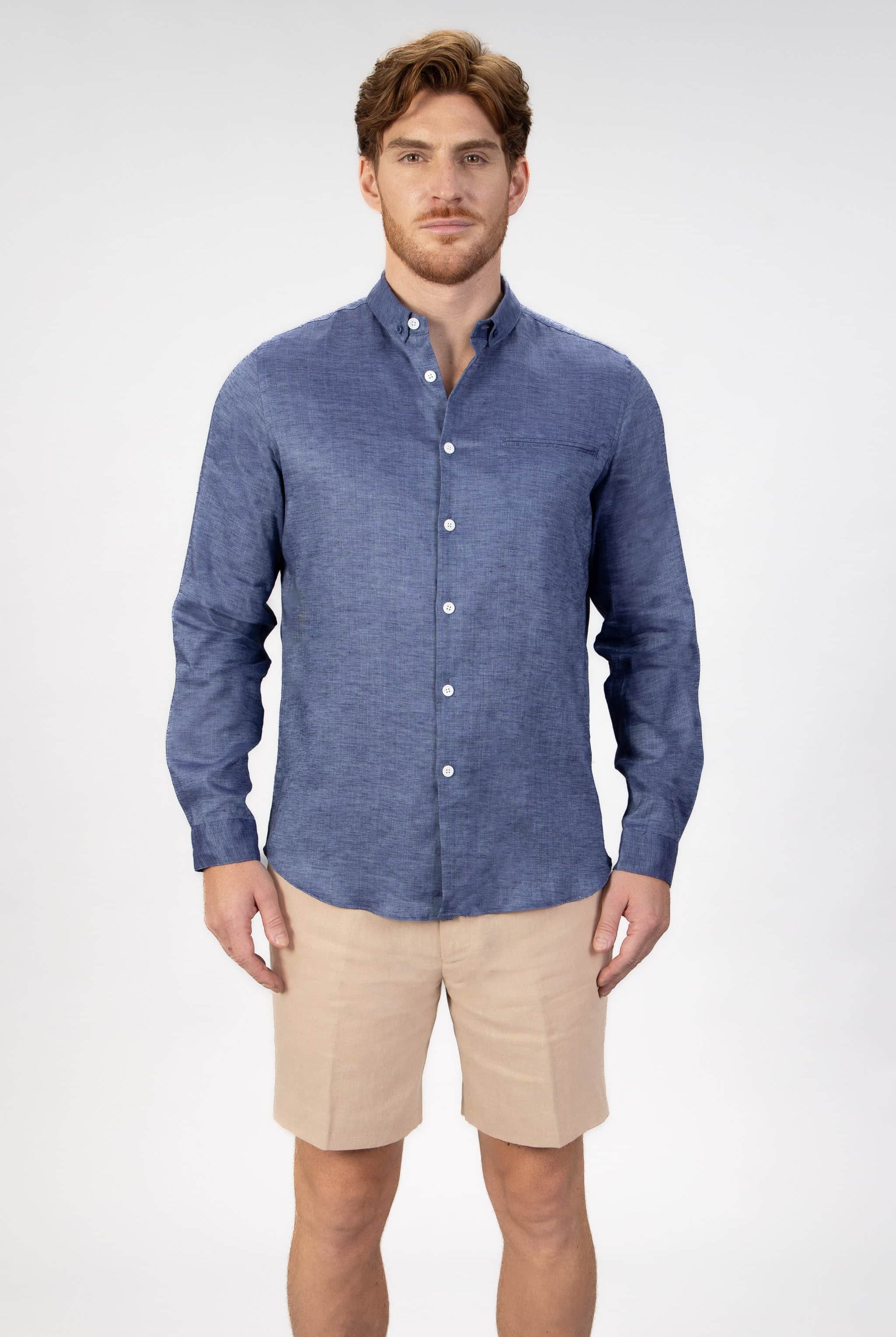 Man wearing a blue button-down shirt and beige shorts on a light gray background