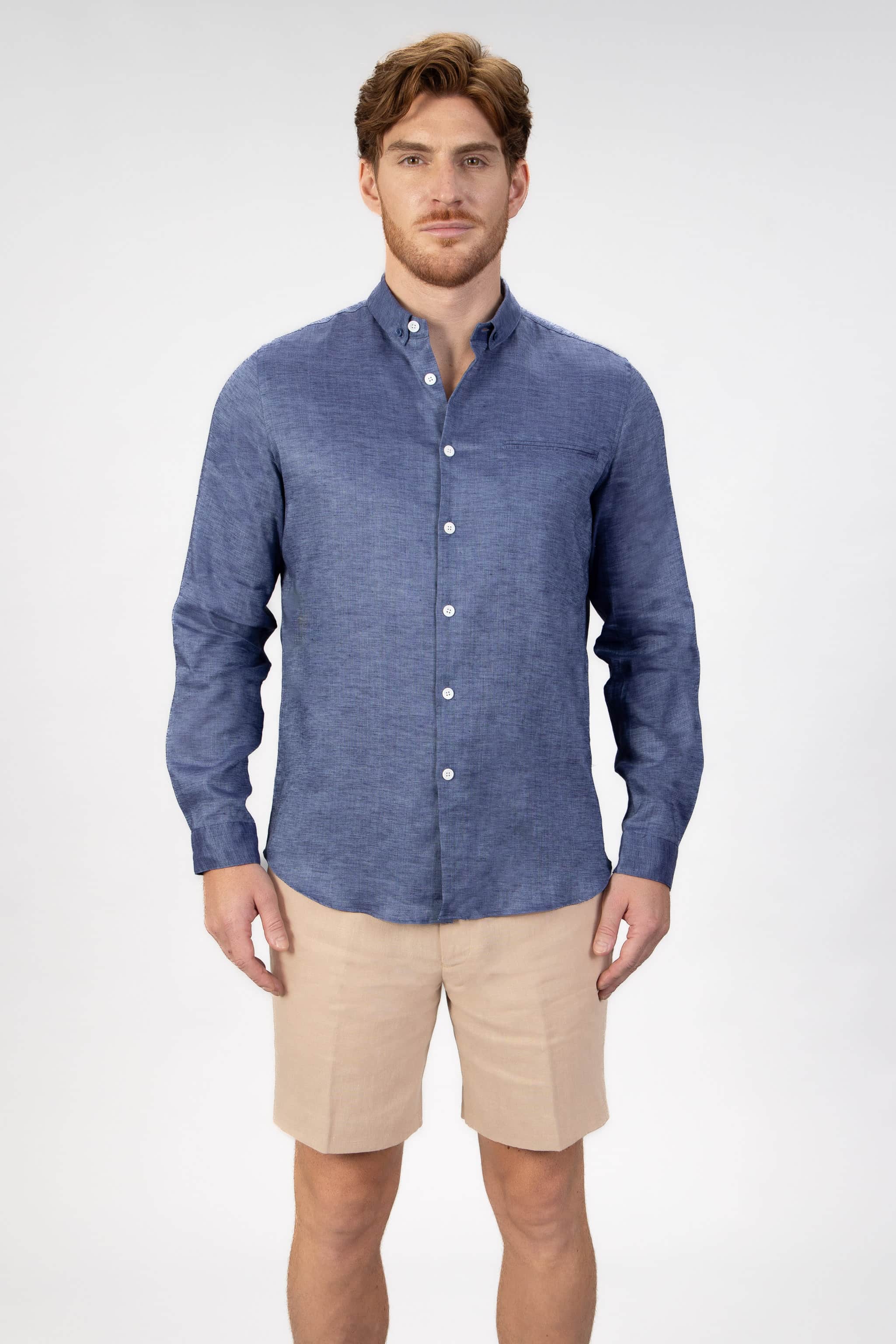 Man wearing a blue button-down shirt and beige shorts on a light gray background