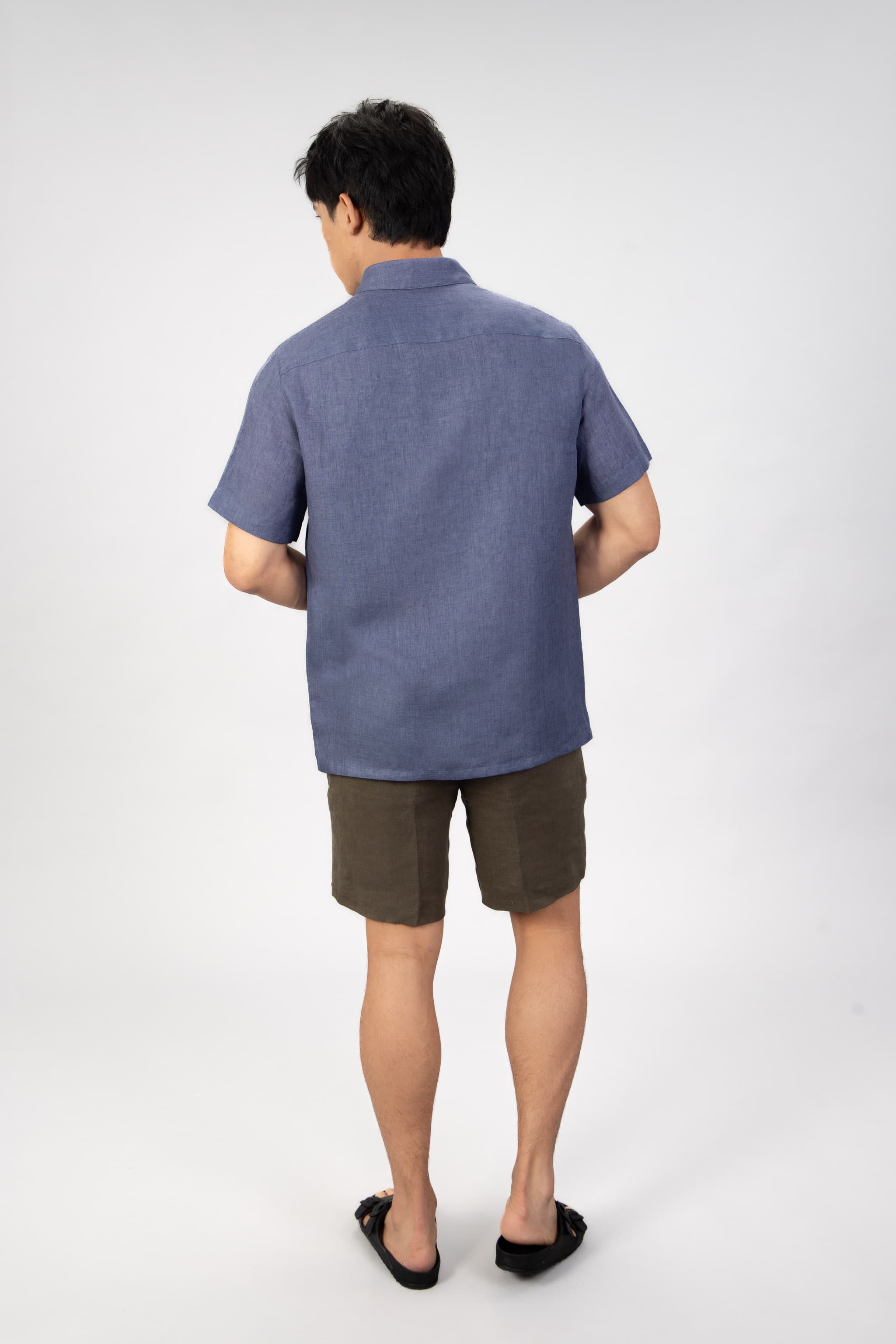 Man wearing a blue linen short sleeve shirt with beige cotton shorts on light gray background
