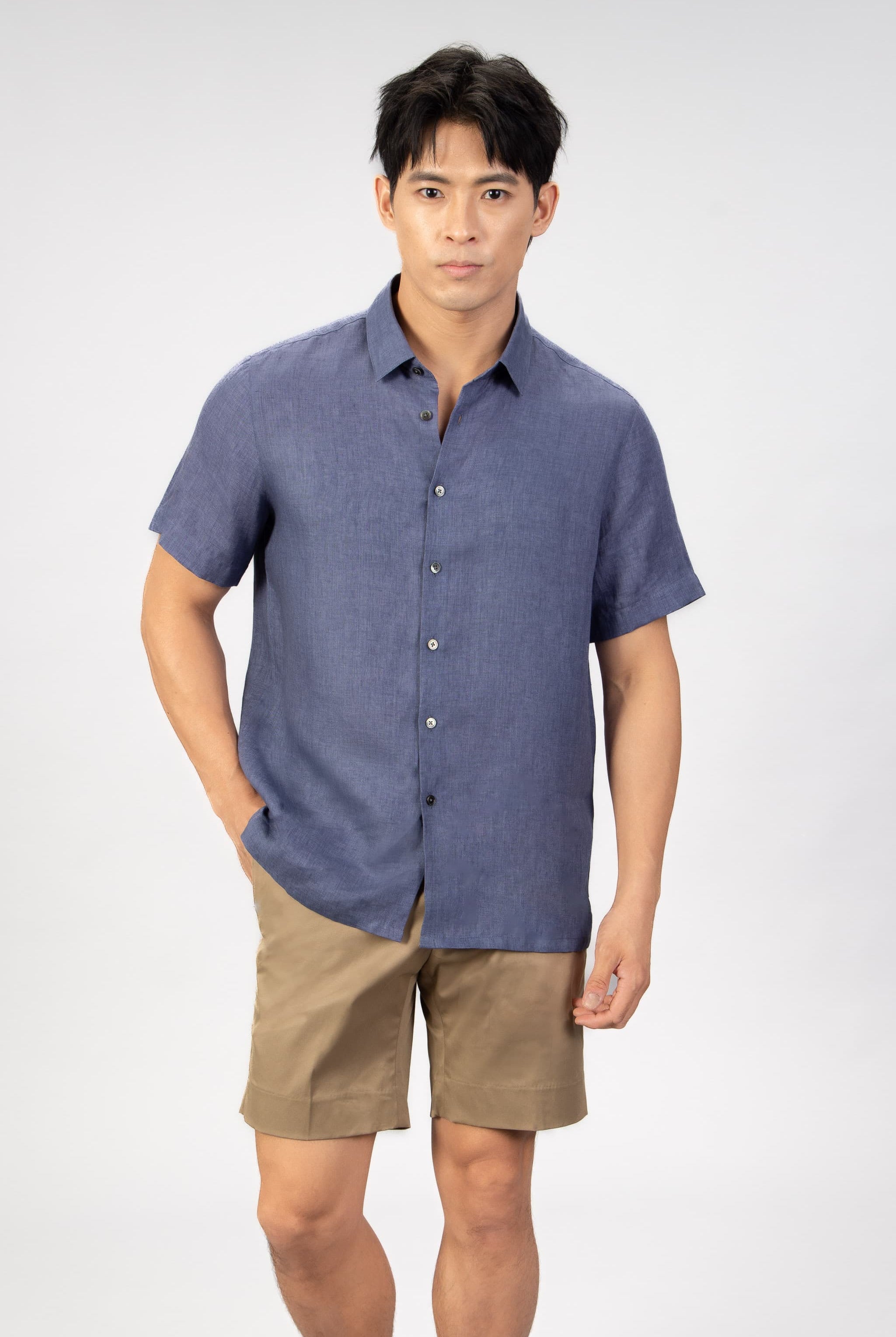 man wearing a blue linen short sleeve shirt with beige cotton shorts on light gray background