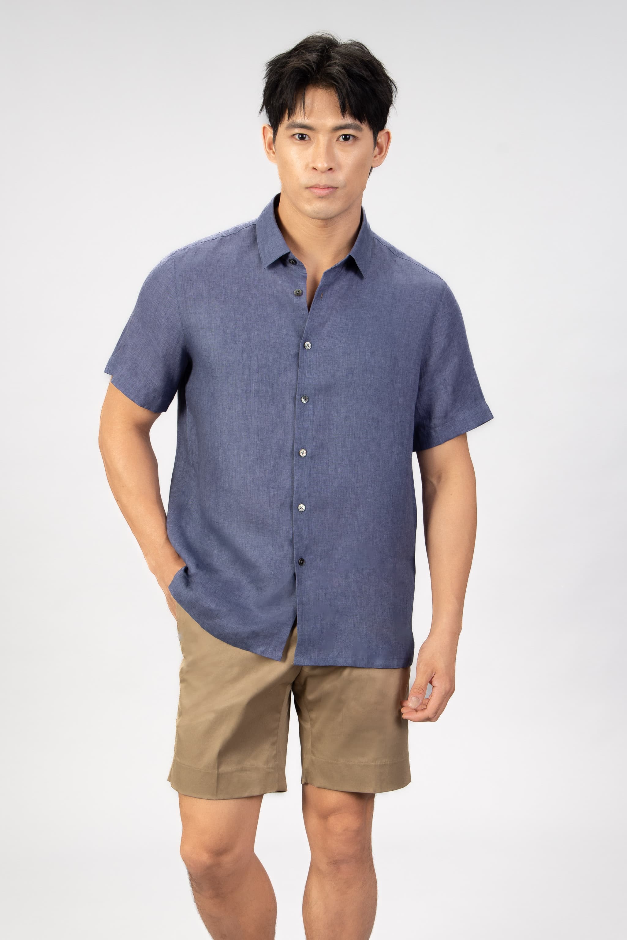 man wearing a blue linen short sleeve shirt with beige cotton shorts on light gray background