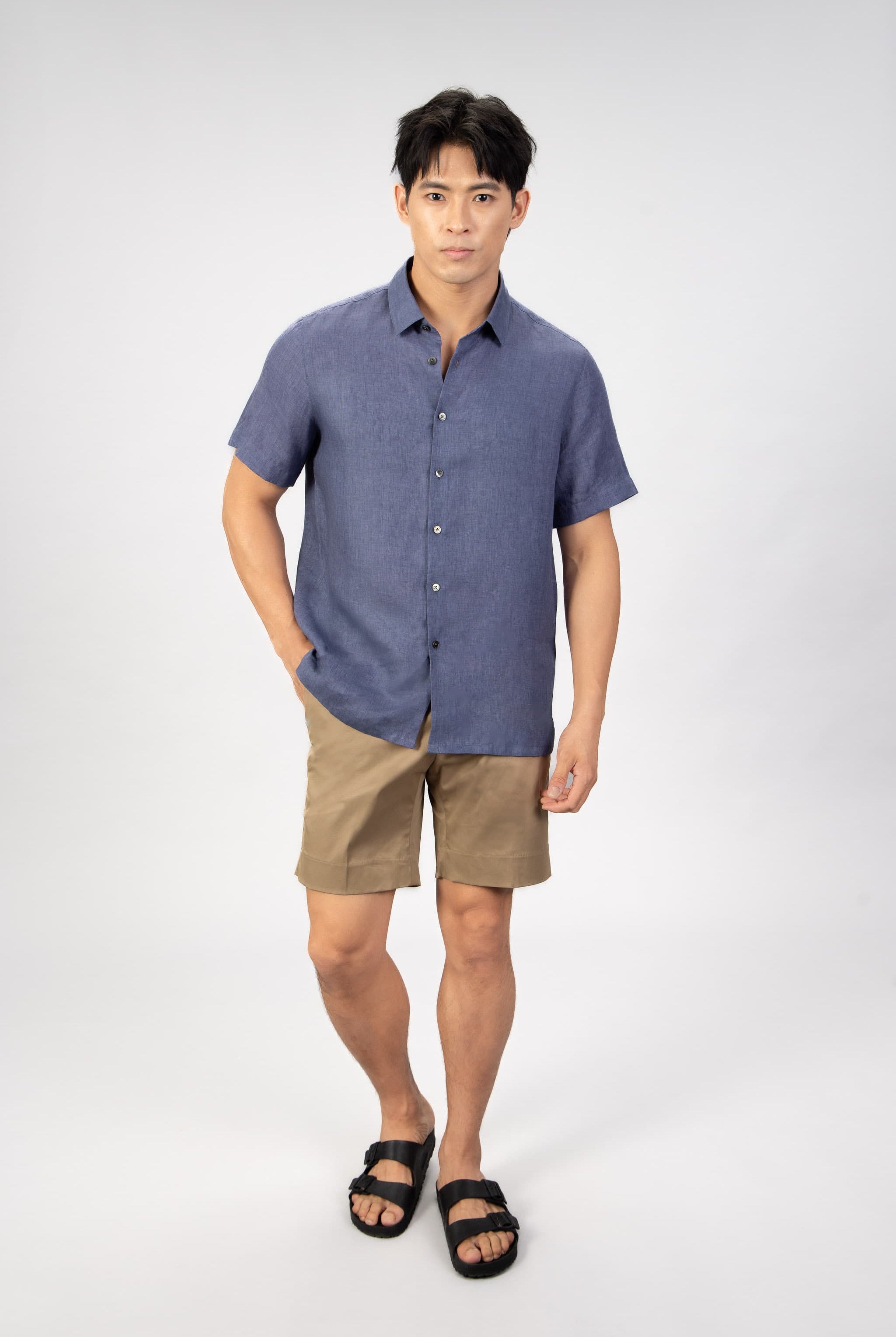 Man wearing a blue shirt and beige shorts on a white background