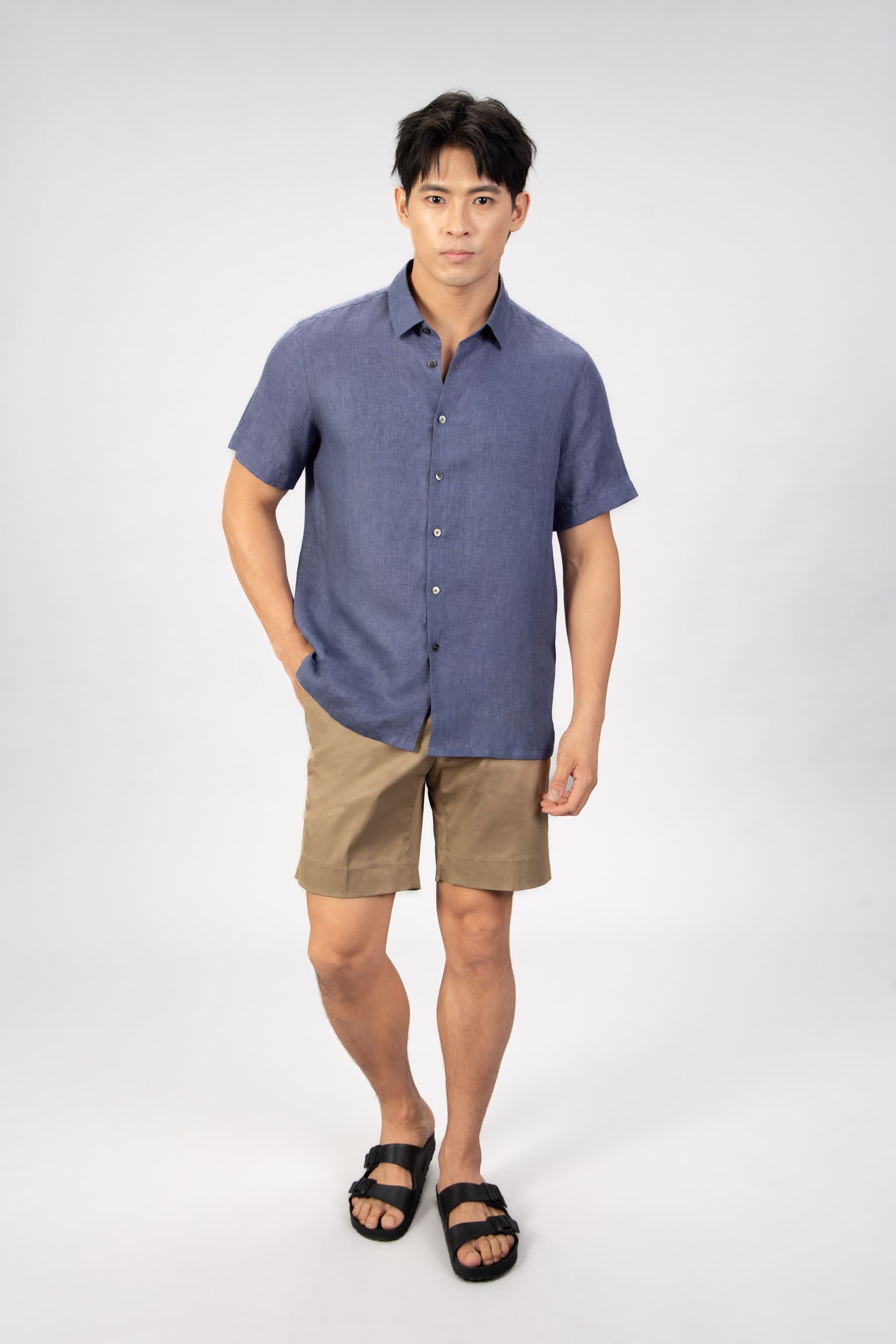 Man wearing a blue shirt and beige shorts on a white background