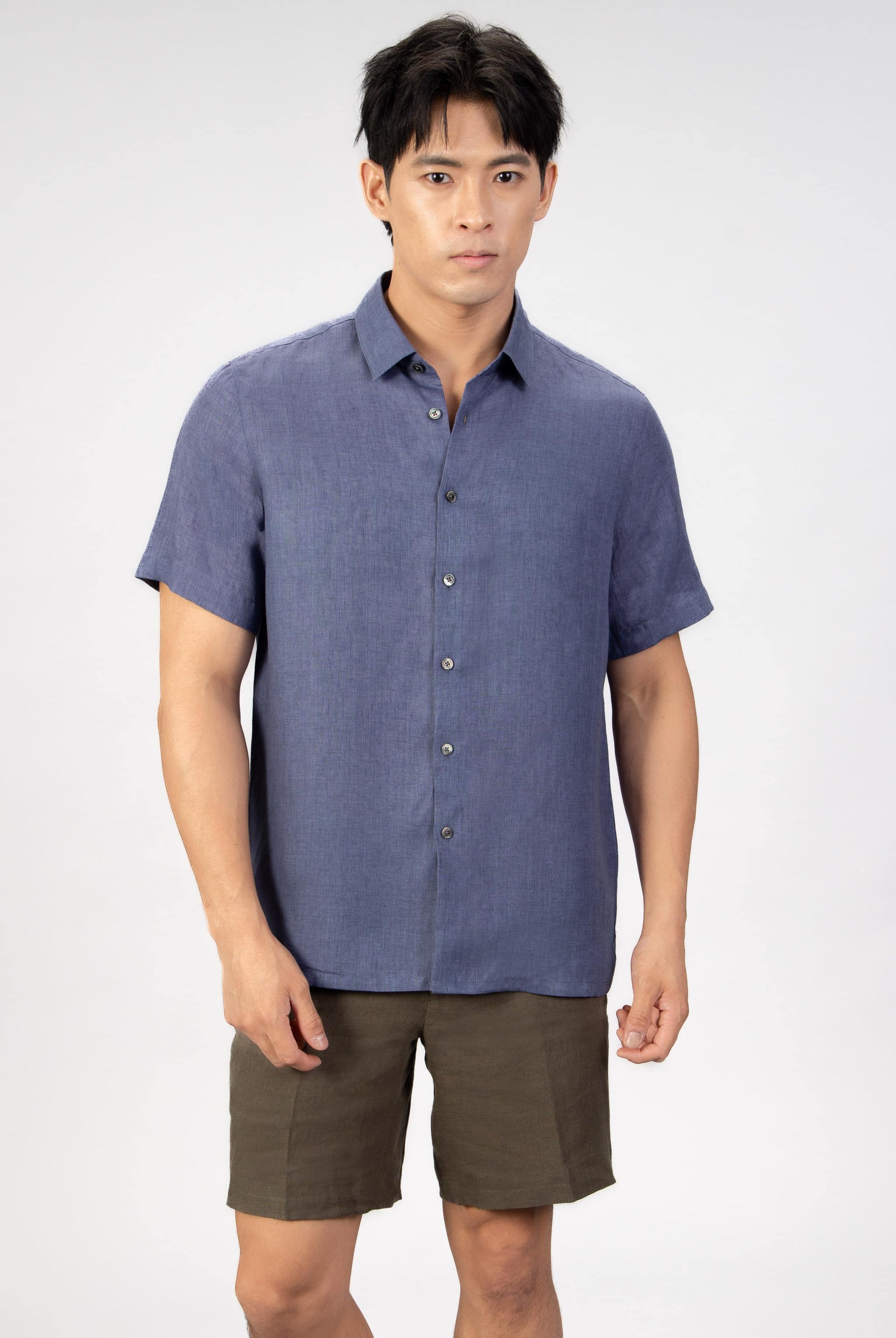 Man wearing a blue linen short sleeve shirt with beige cotton shorts on light gray background