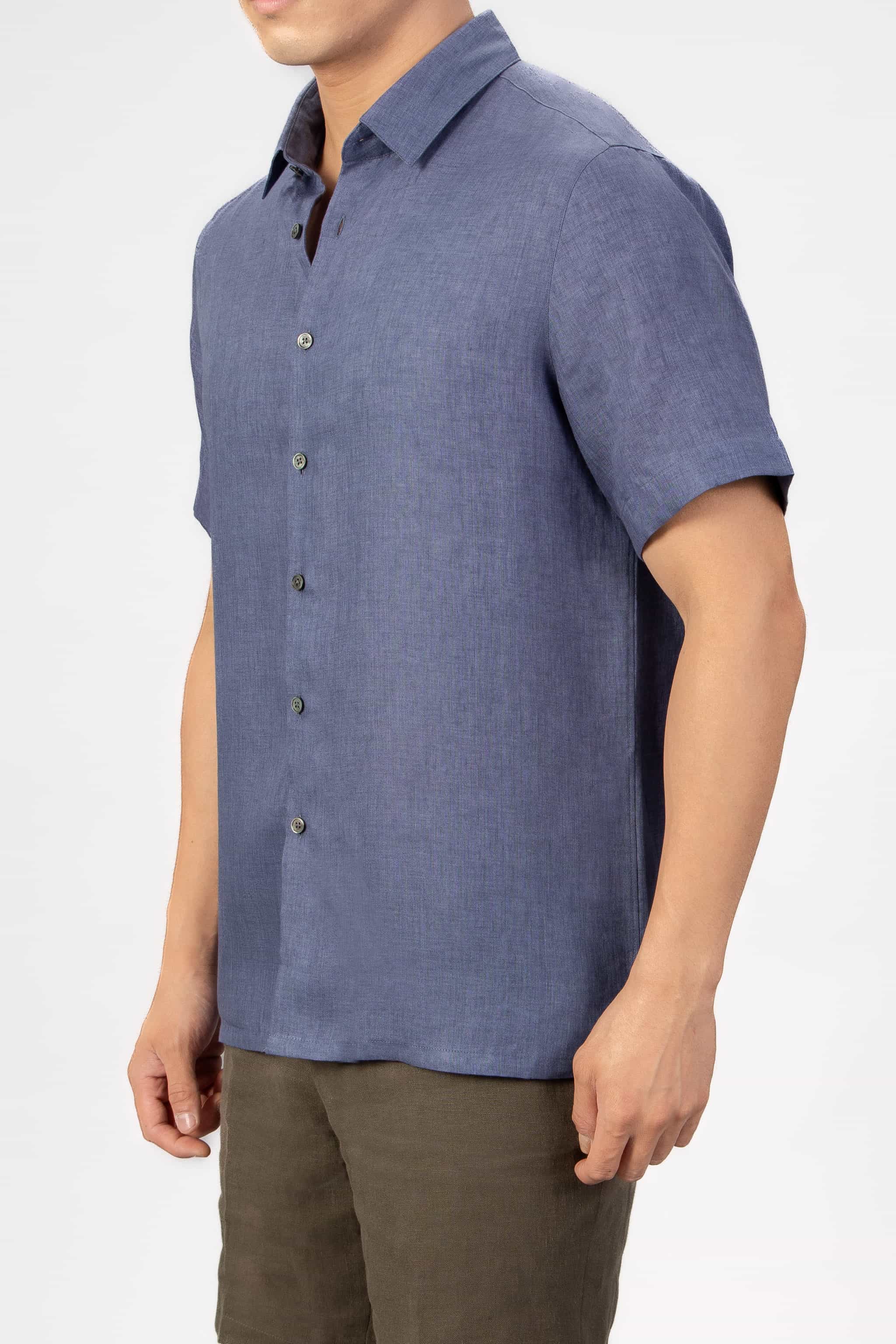 Man wearing a blue linen short sleeve shirt with beige cotton shorts on light gray background