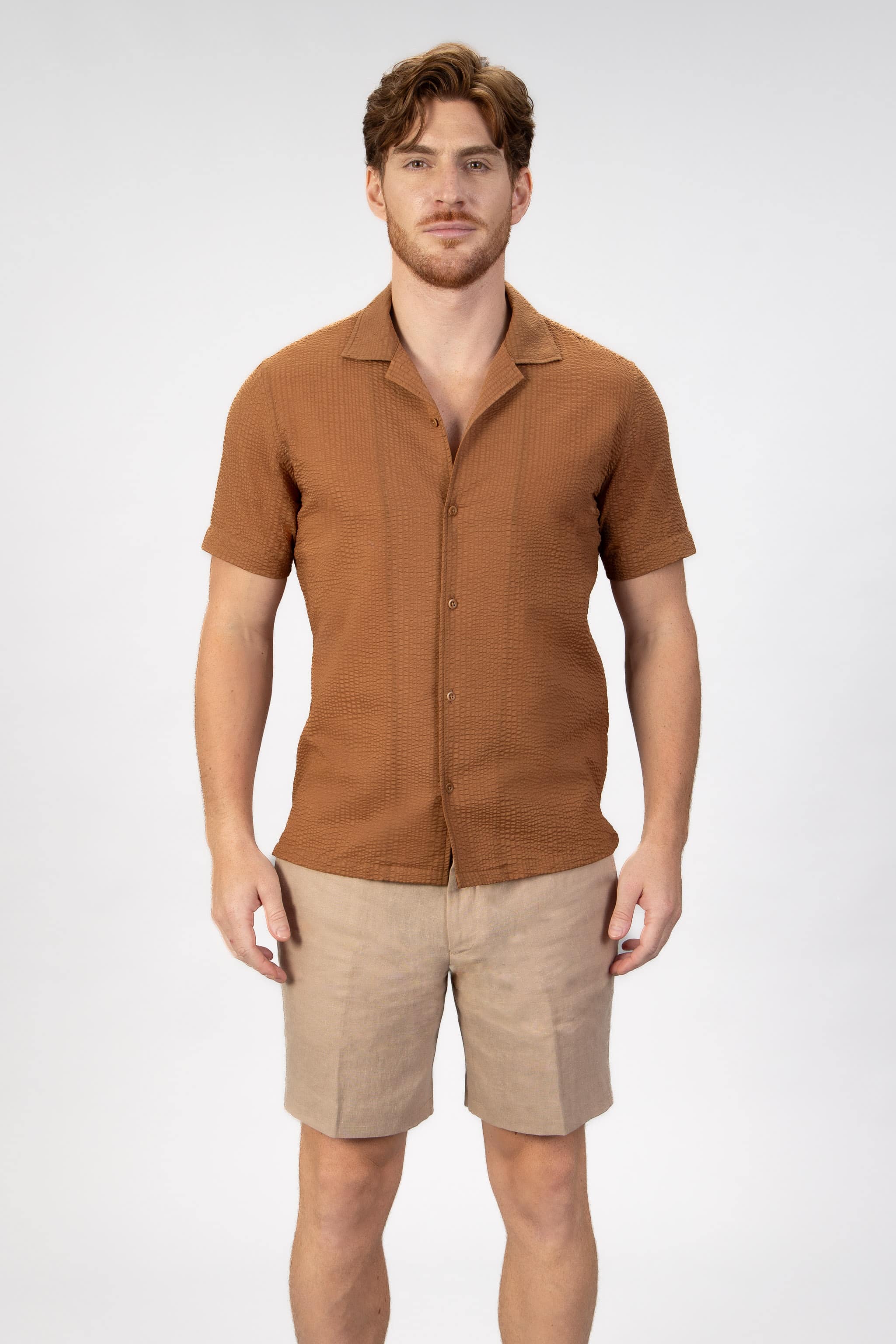 Man wearing a brown textured shirt and beige shorts on a light gray background