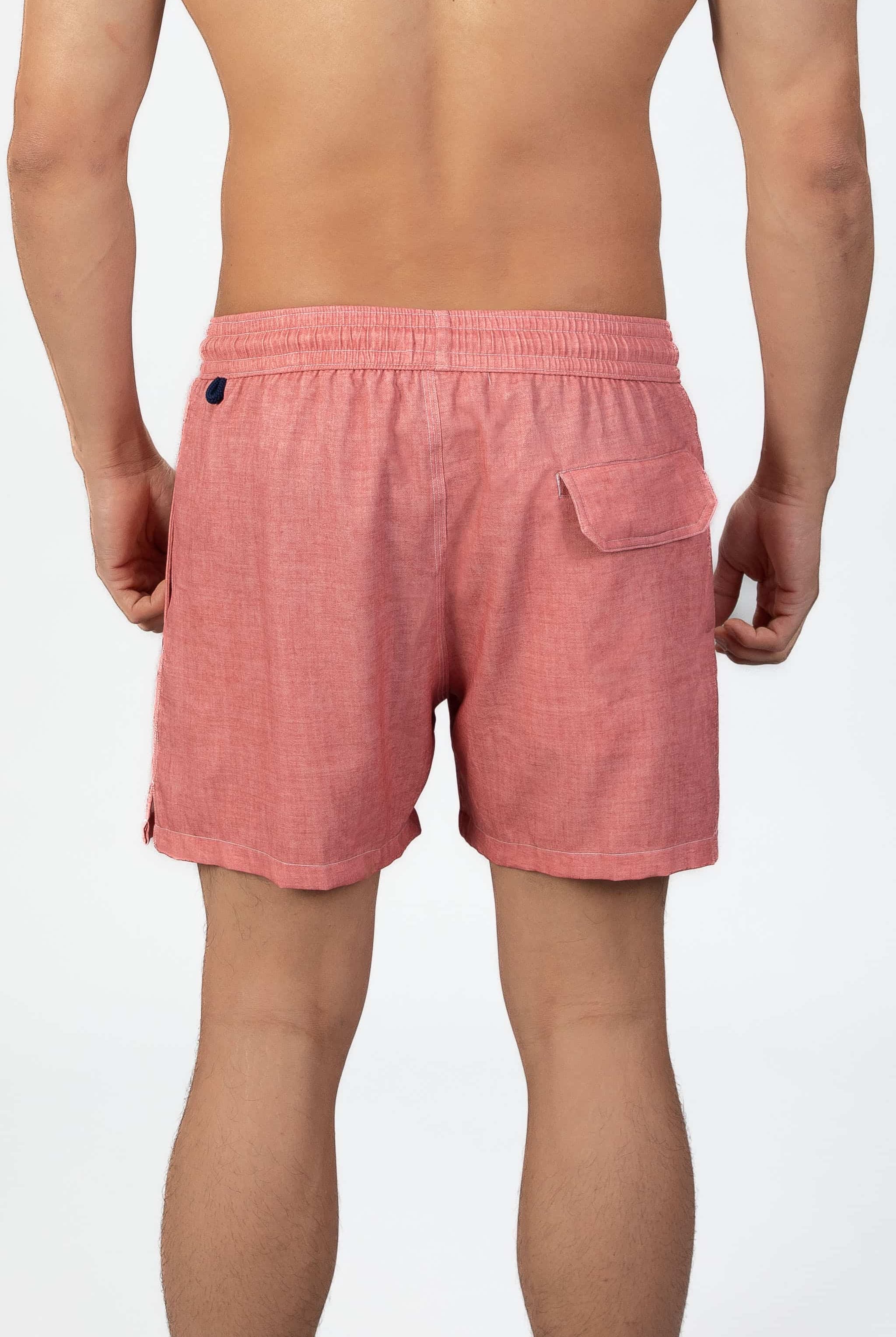 Man wearing pink-coral soft swim shorts with magnet closure back pocket on a light gray background