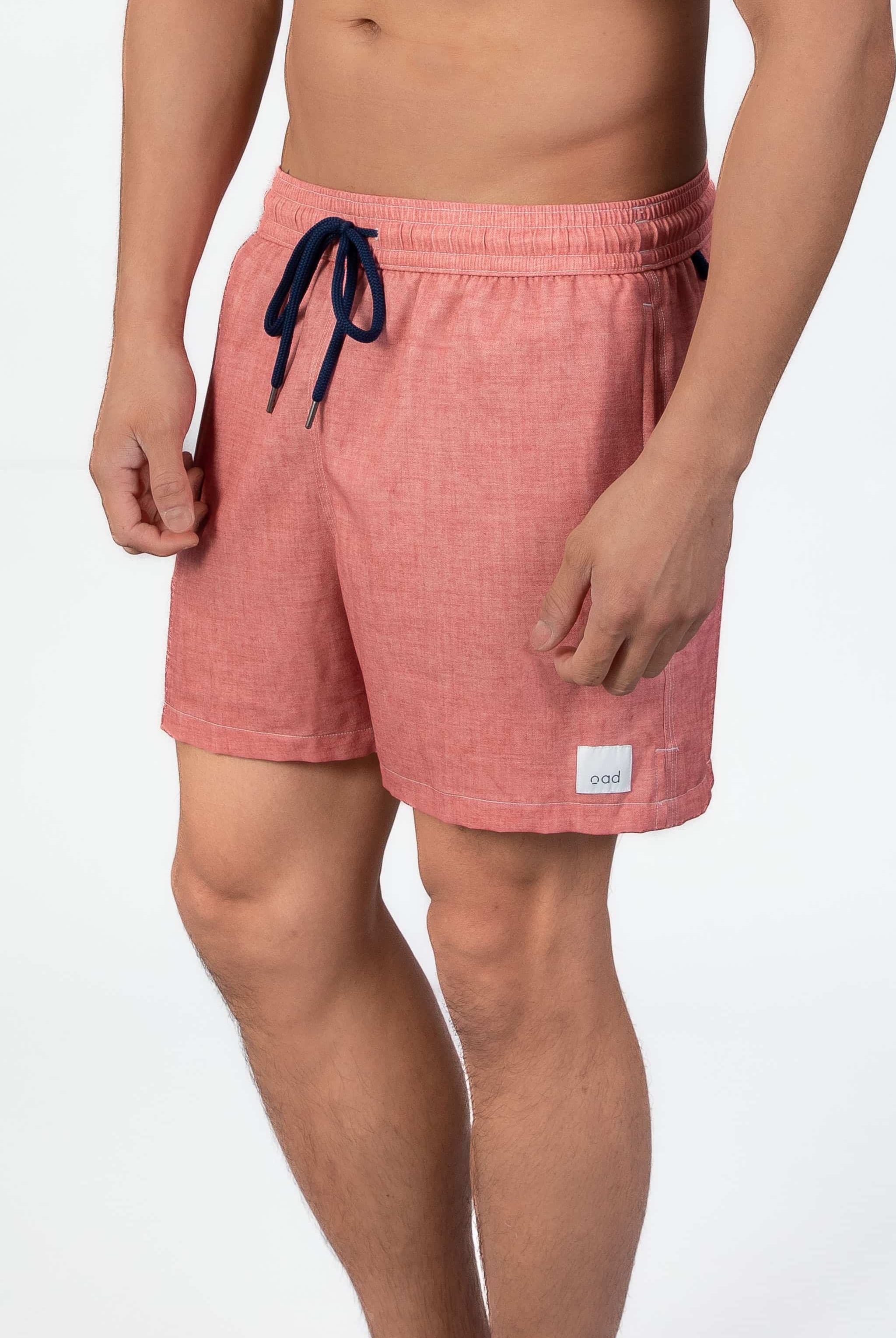 Man wearing pink-coral soft swim shorts with a drawstring in navy on a light gray background