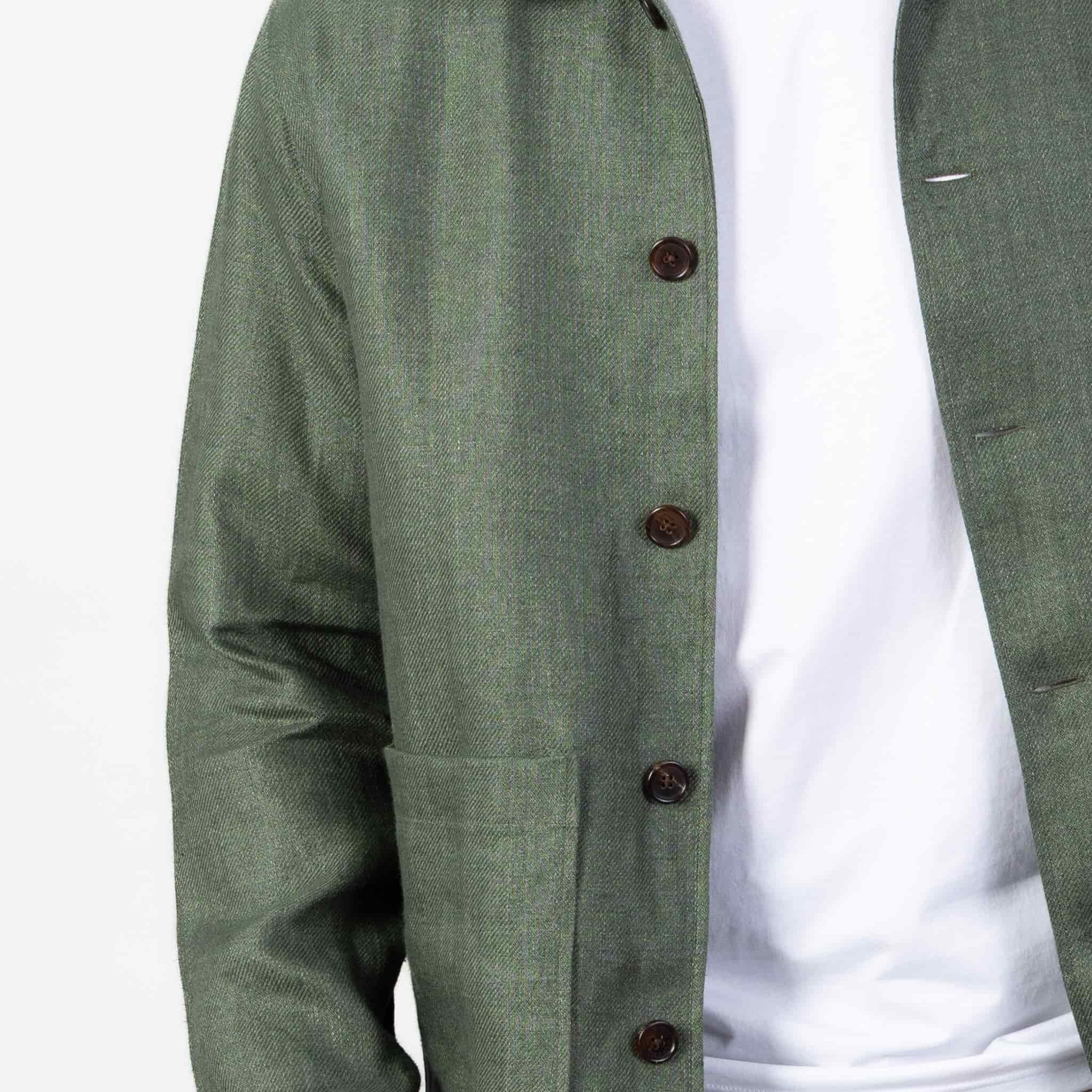 Person wearing a green linen overshirt over a white T-shirt with beige chinos on a light gray background