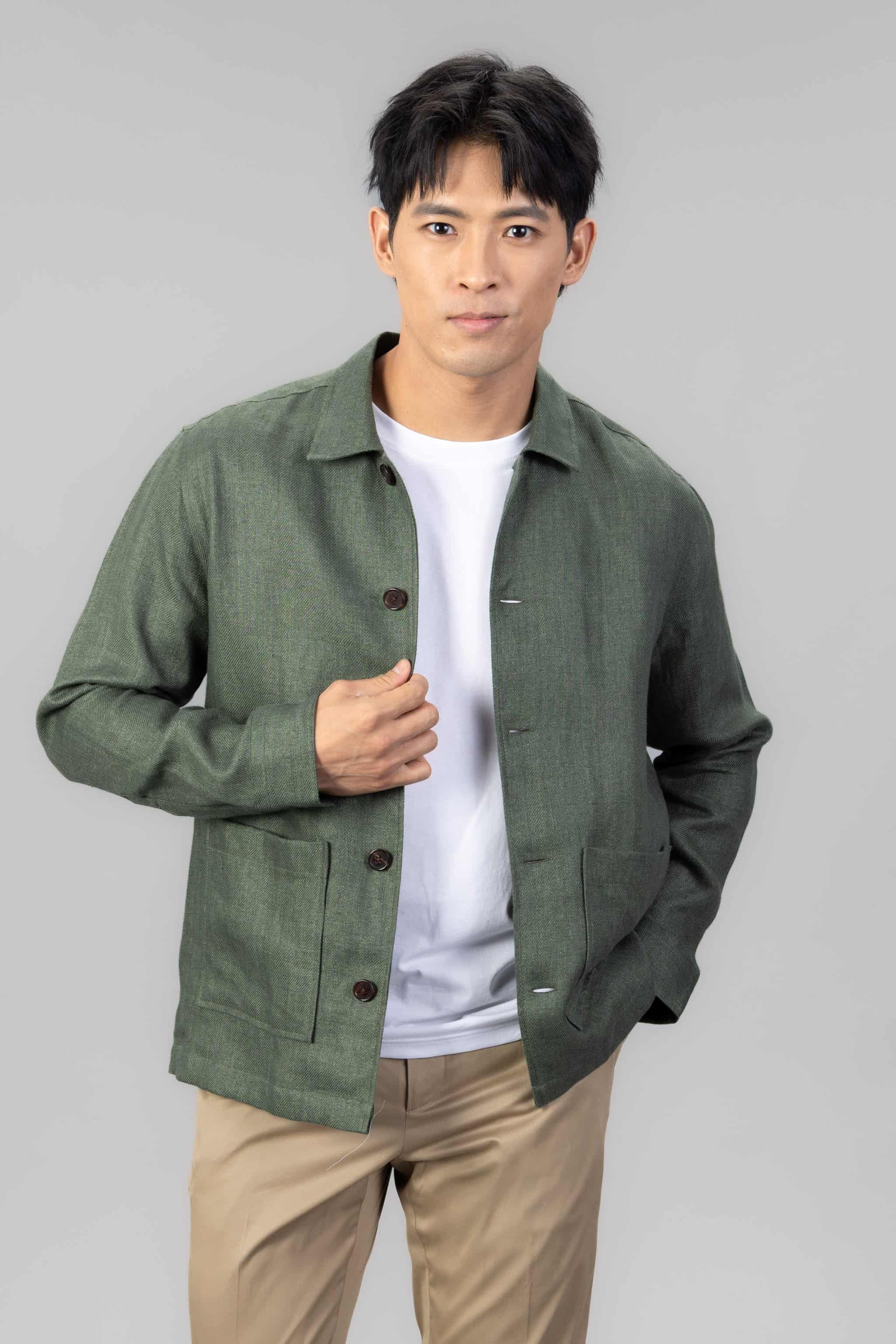 Person wearing a green linen overshirt over a white T-shirt with beige chinos on a light gray background