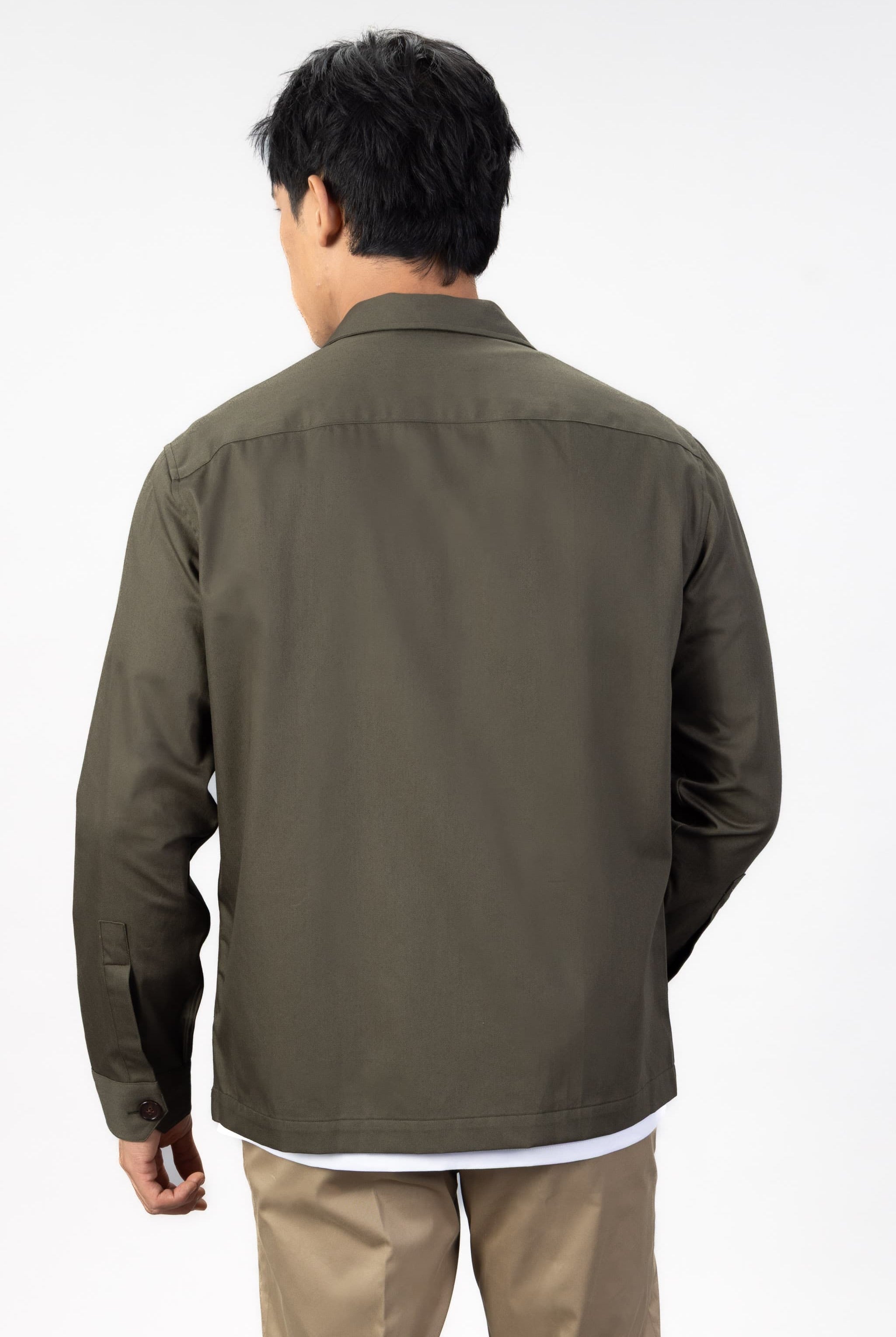 Person wearing a green over shirt over a white T-shirt with beige chinos on a light gray background