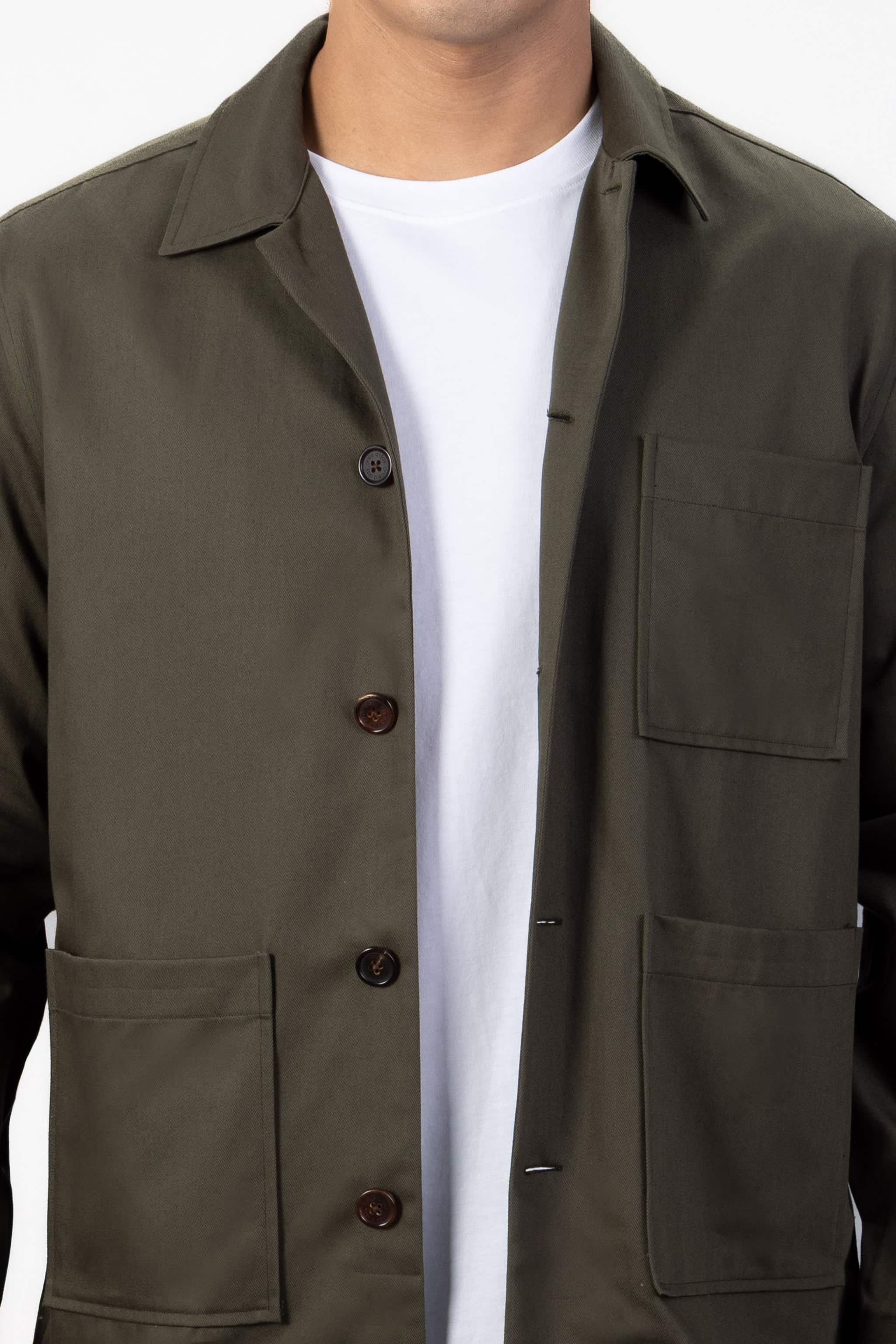 Model wearing a green over shirt over a white T-shirt with beige chinos on a light gray background