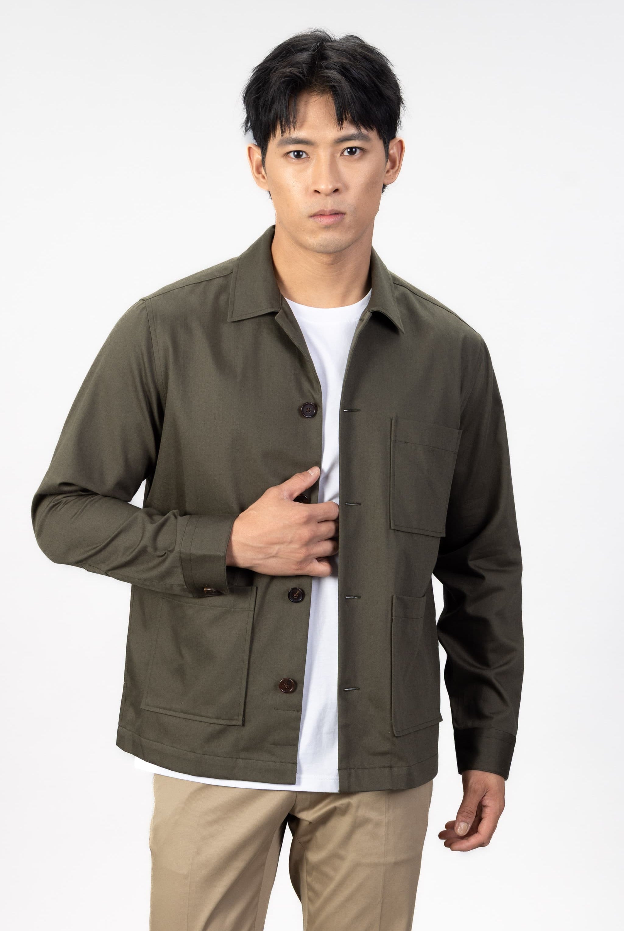 Man wearing a green over shirt over a white T-shirt with beige chinos on a light gray background