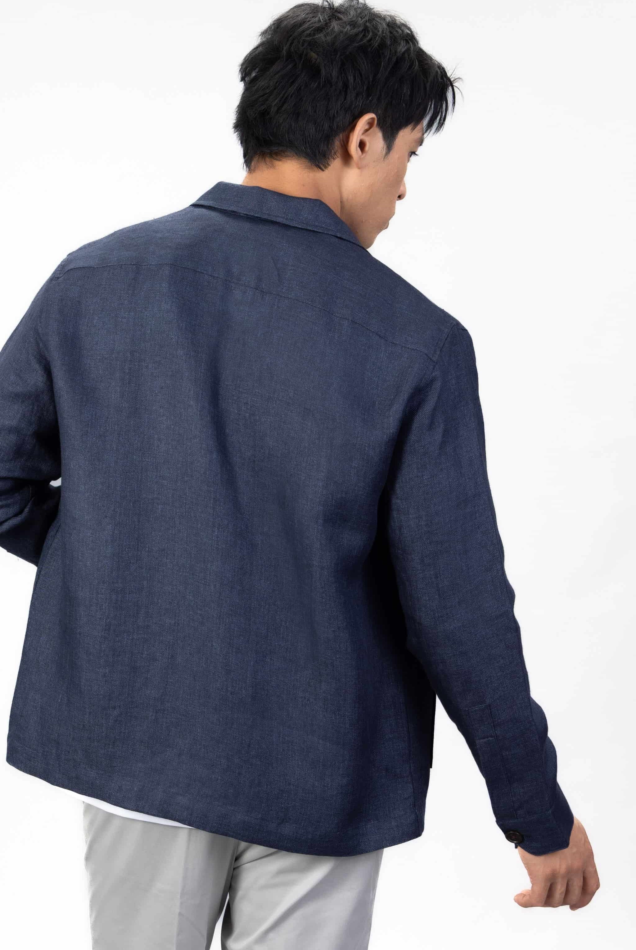 Person wearing a navy blue linen overshirt with gray chinos on a light gray background