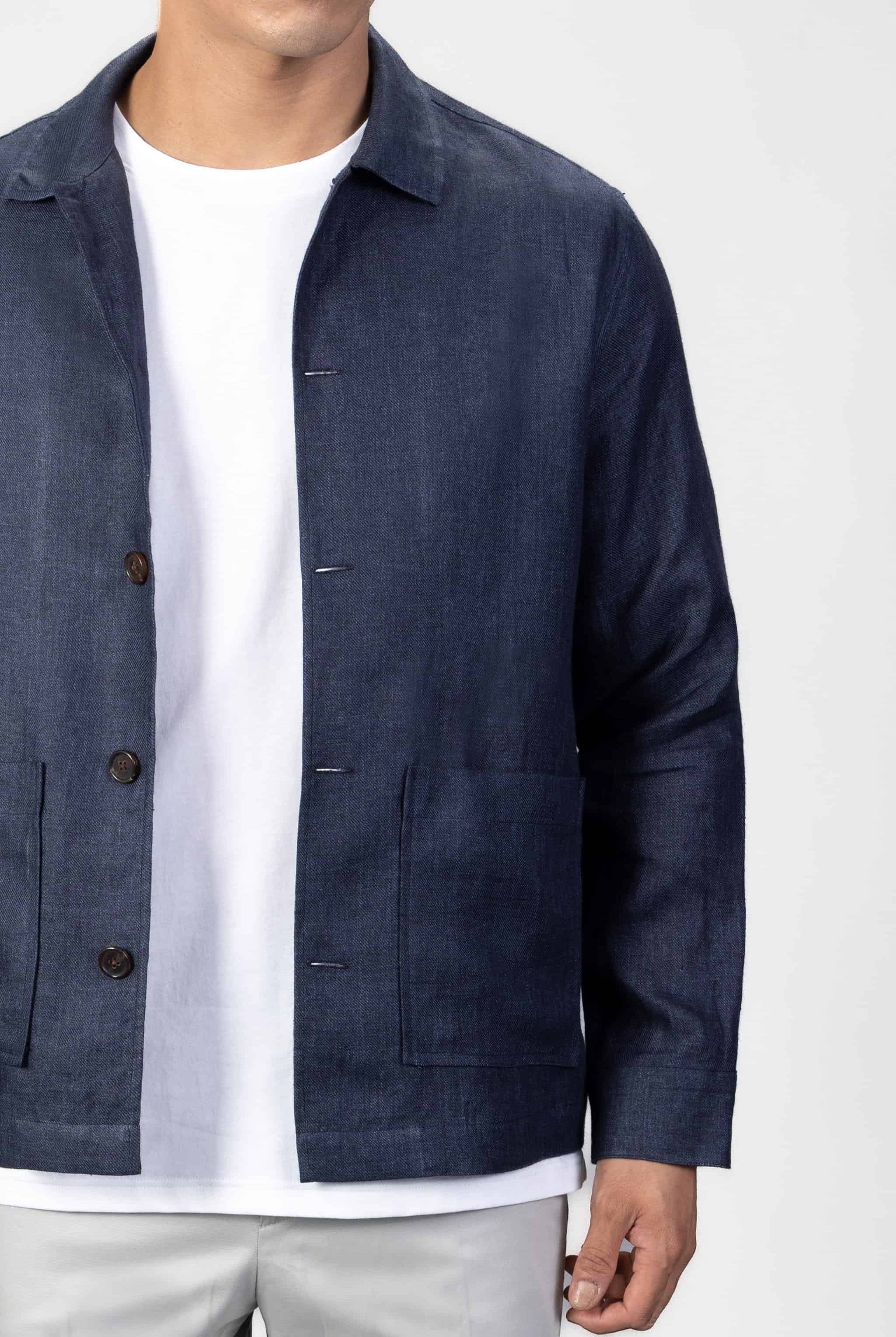 Man wearing a navy blue linen overshirt over a white T-shirt with gray chinos on a light gray background