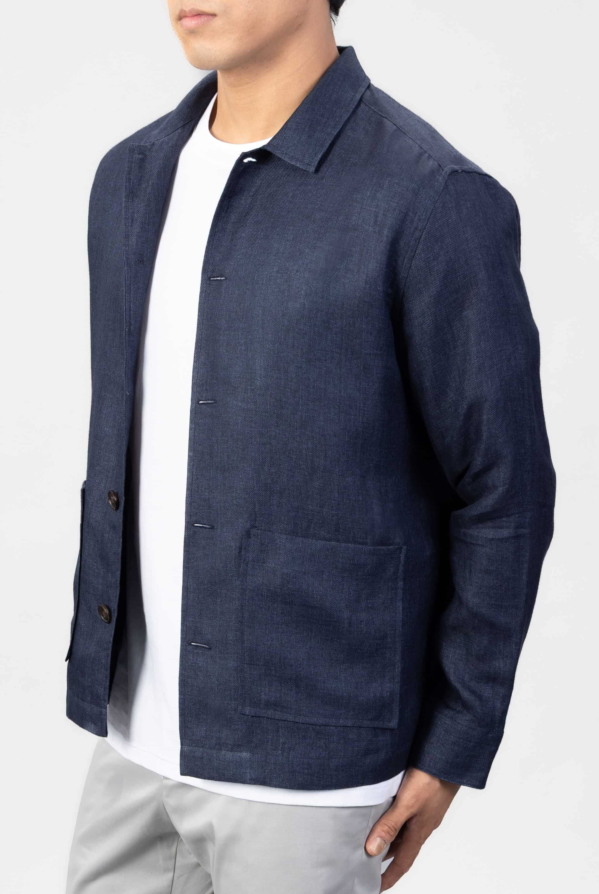 Man wearing a navy blue linen overshirt over a white T-shirt with gray chinos on a light gray background