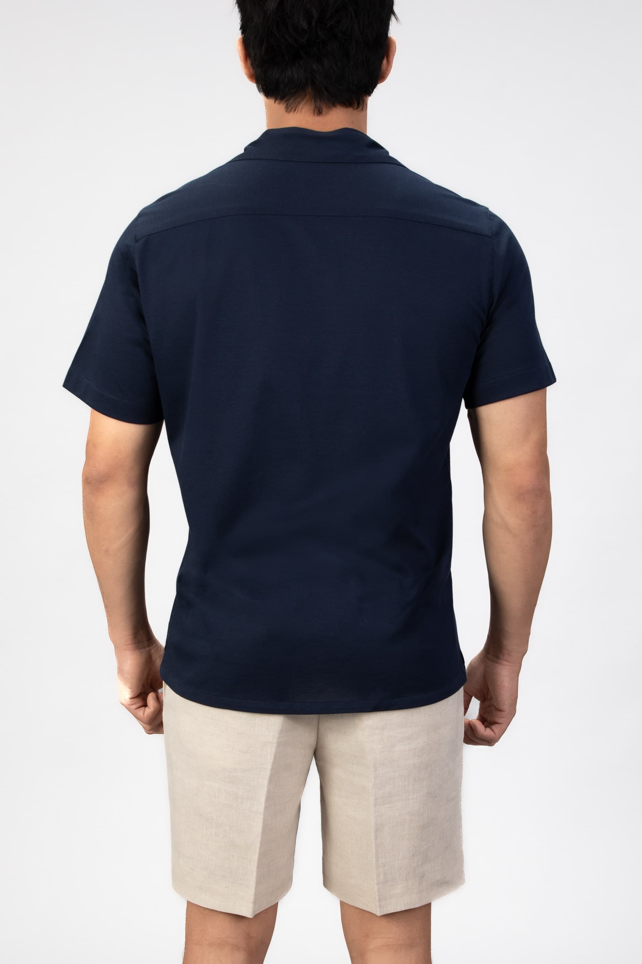 Person wearing a navy polo shirt and beige shorts on a white background