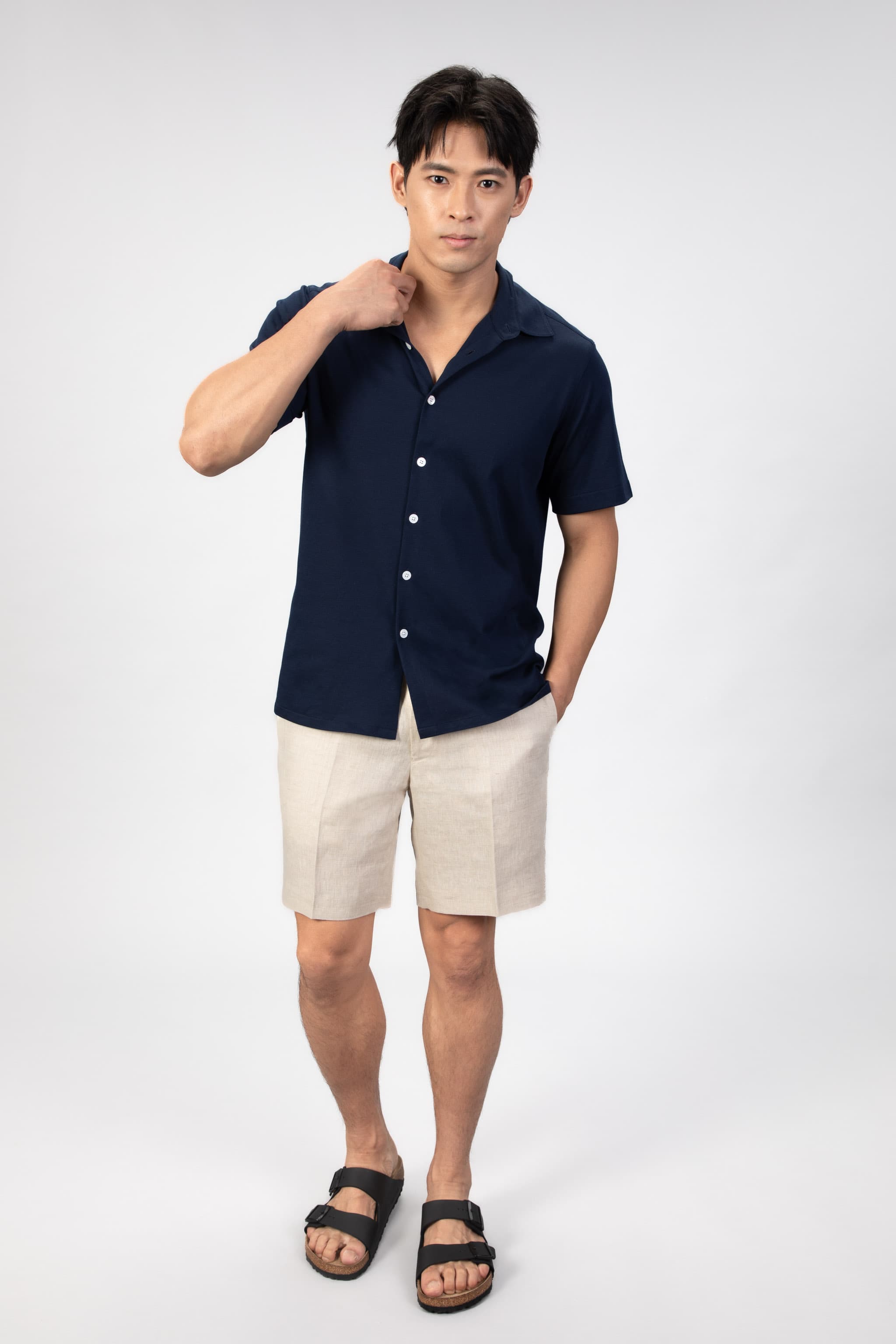 Man wearing a navy shirt and beige linen shorts on a light gray background