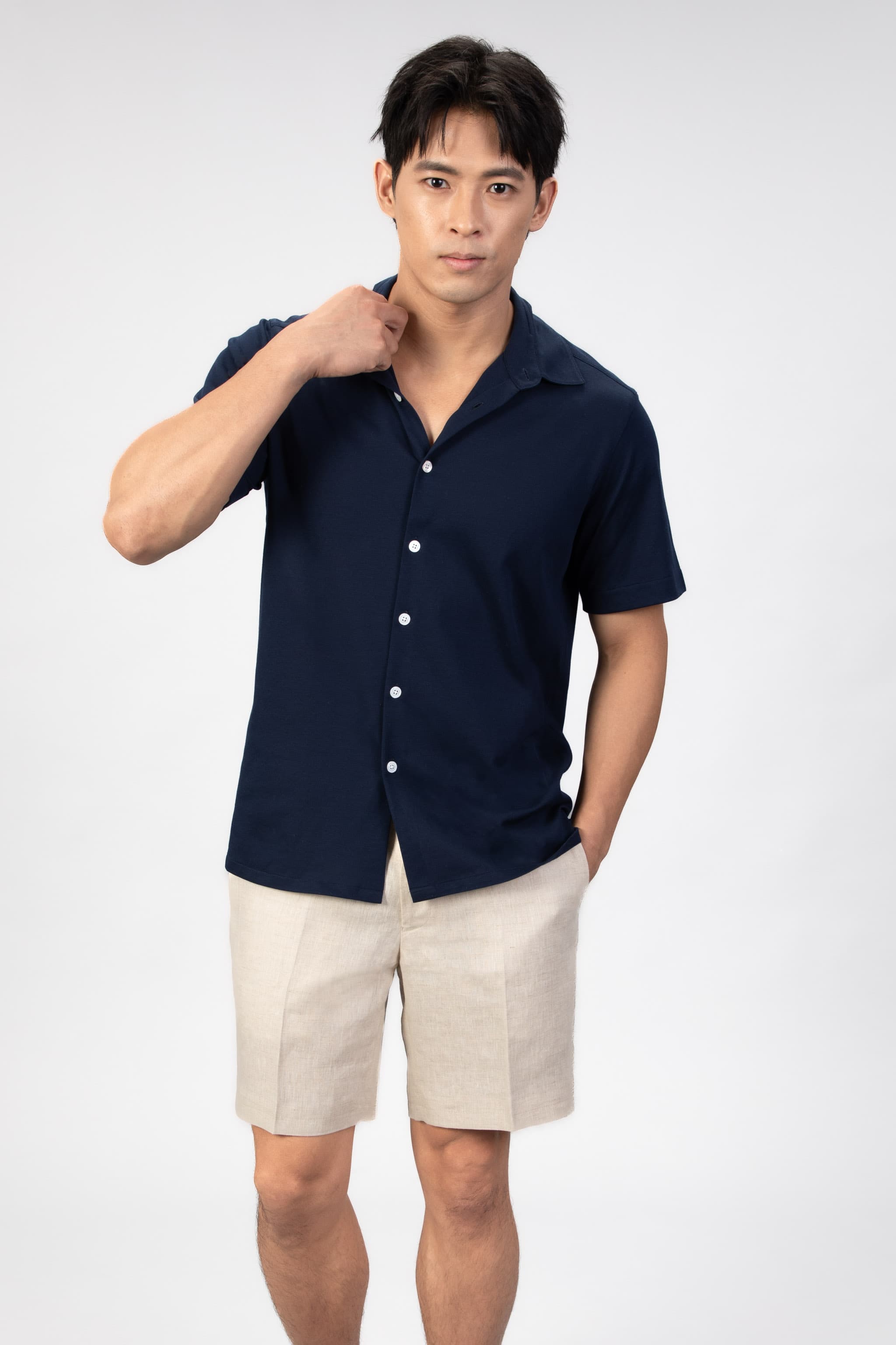 Man wearing a navy short-sleeve shirt and beige shorts on a white background