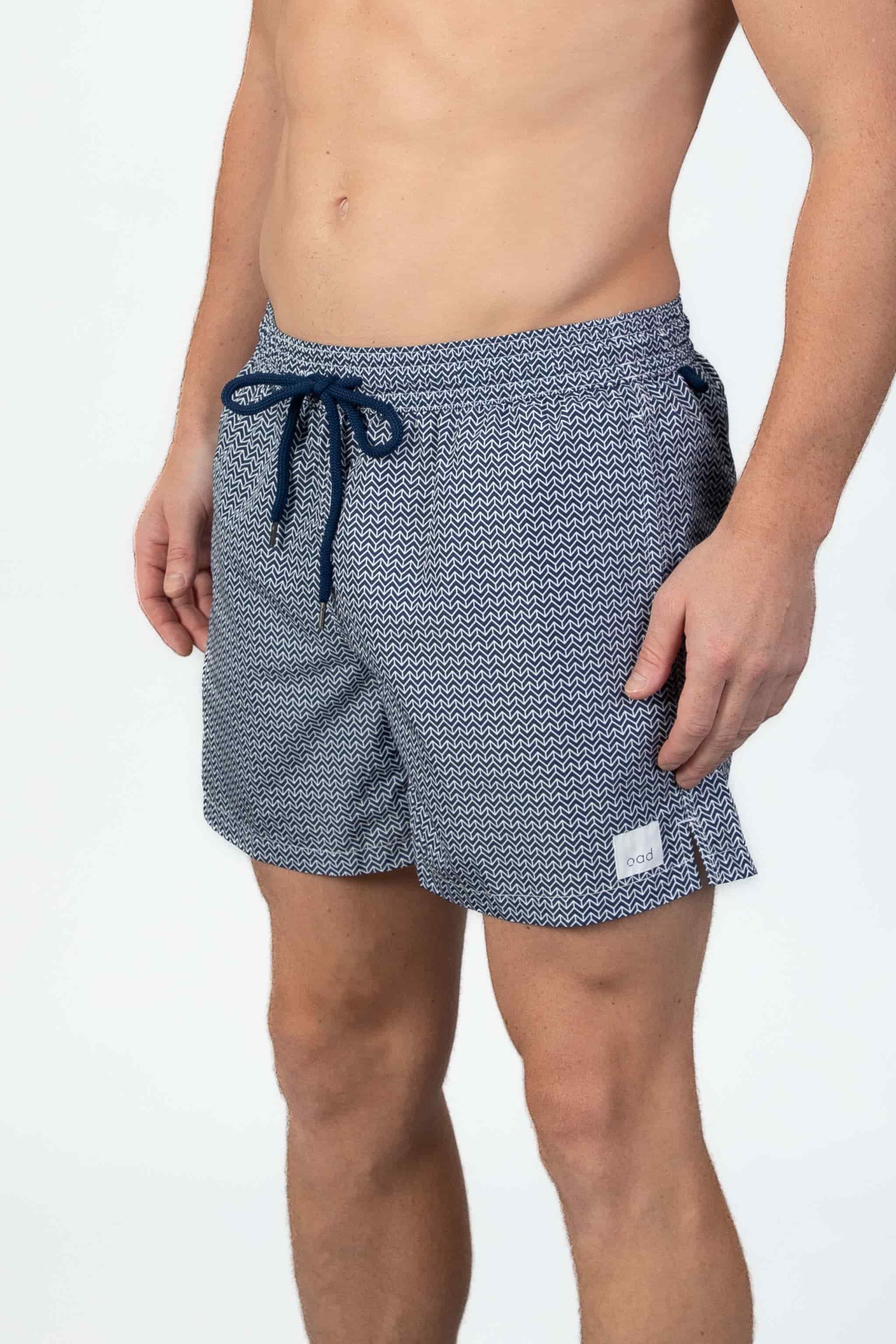 Side view of person wearing classic high end navy swim shorts with a white pattern and drawstring