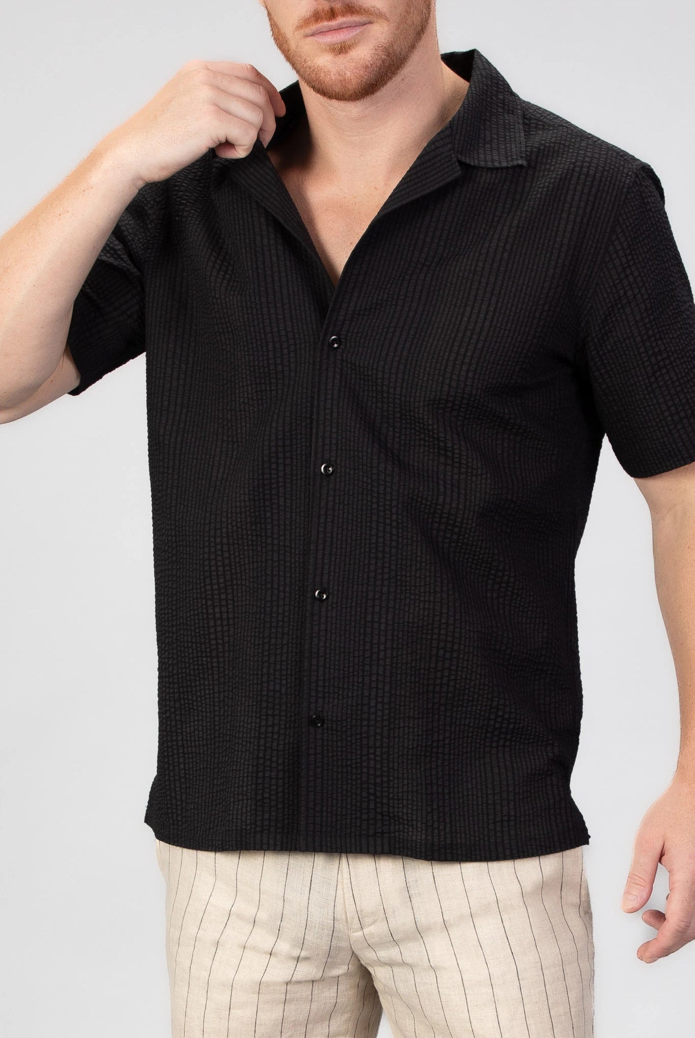 Man wearing a black short-sleeve shirt with a seersucker pattern on a white background