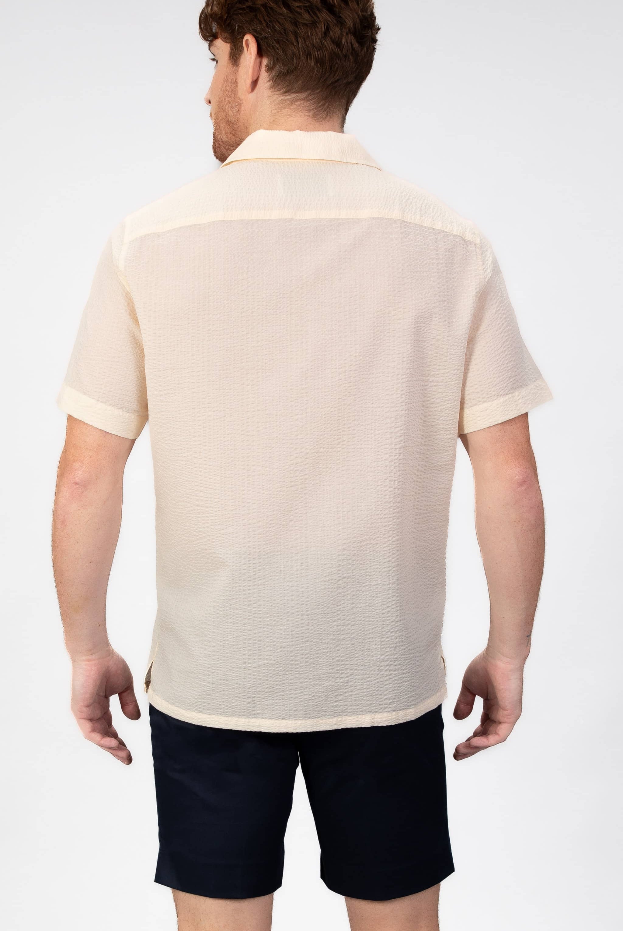 Man wearing a beige-yellow seersucker camp collar shirt on light gray background