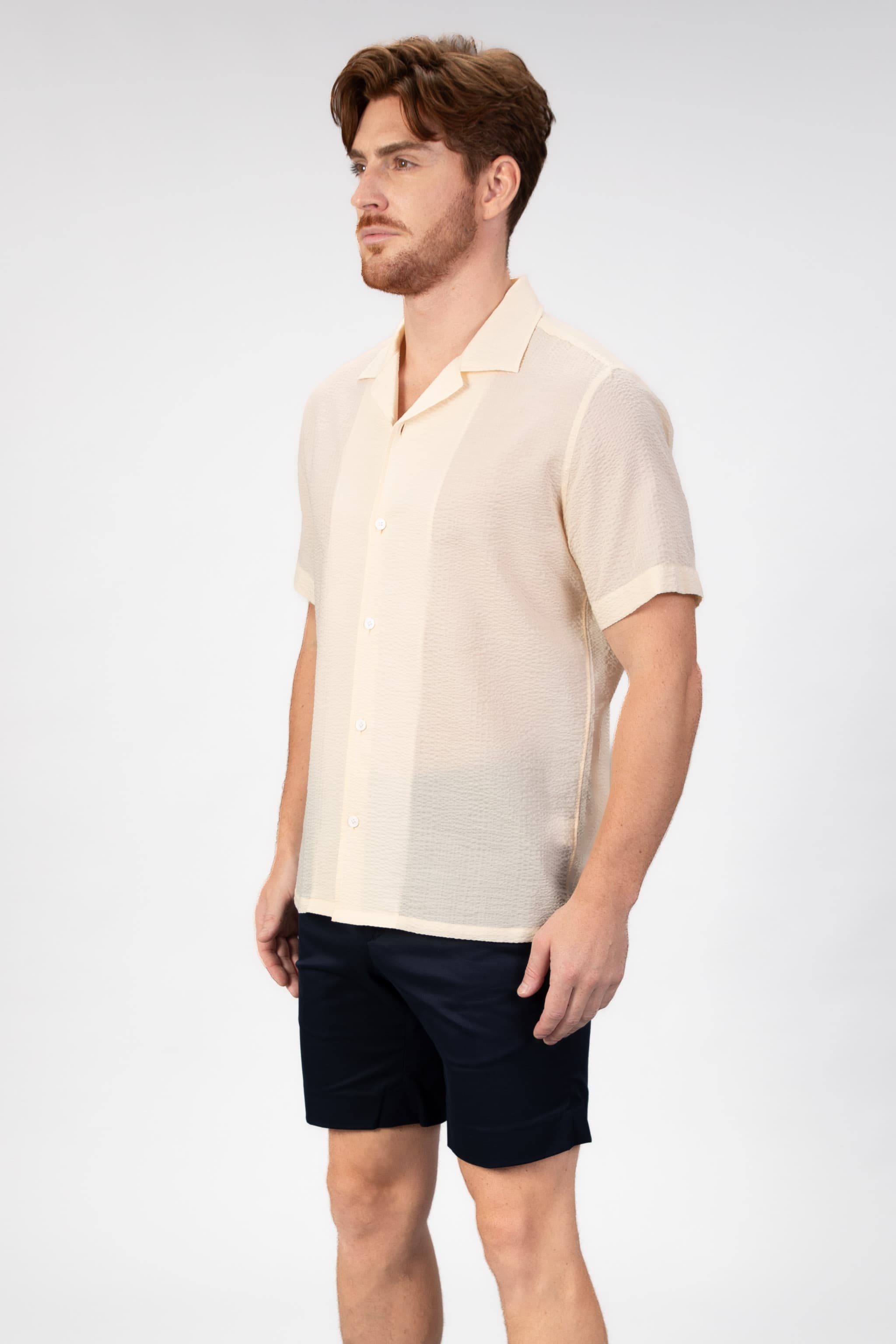 Person wearing a beige-sand seersucker camp collar shirt on light gray background