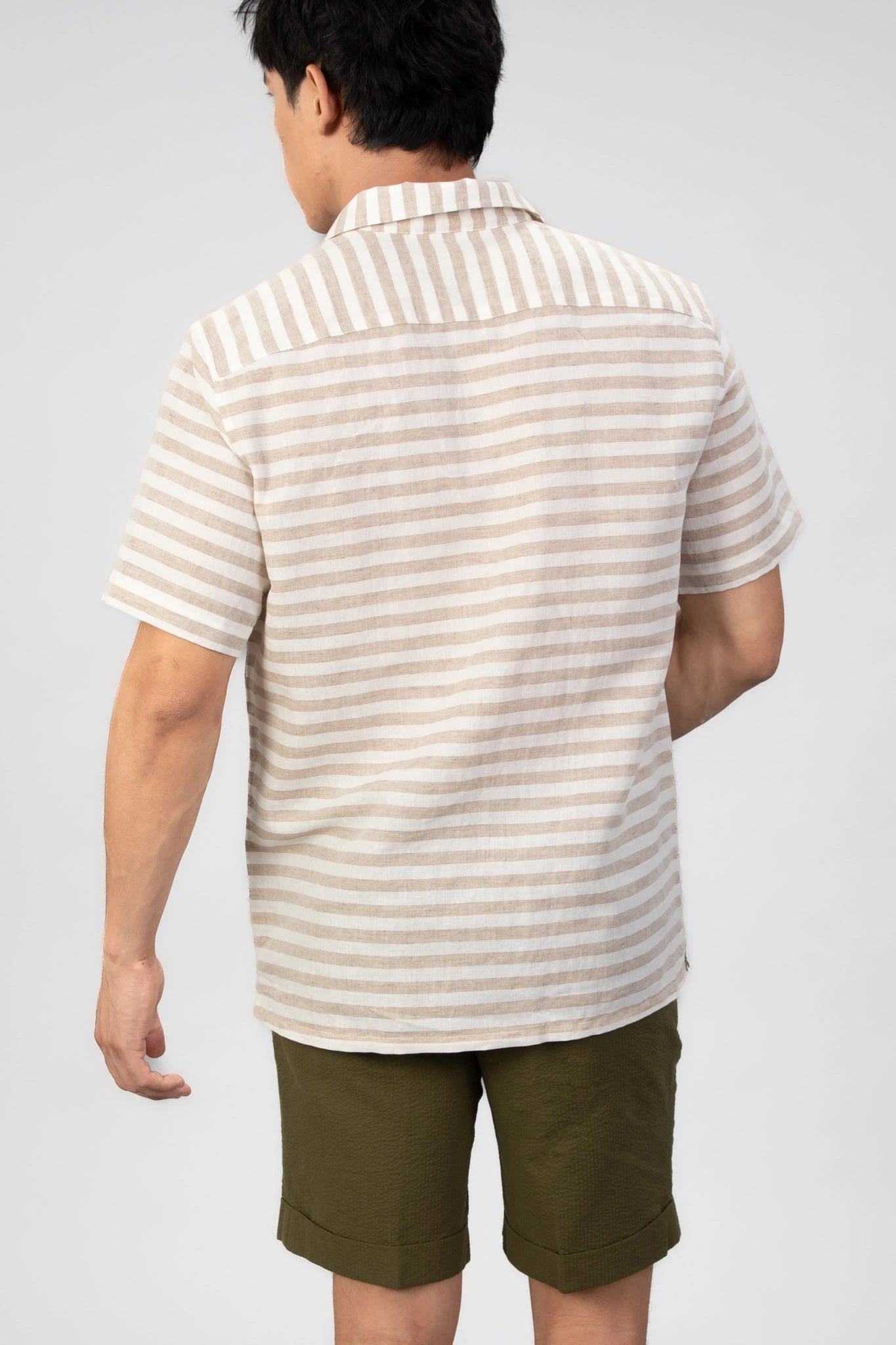 Man wearing a striped shirt and green shorts against a gray background