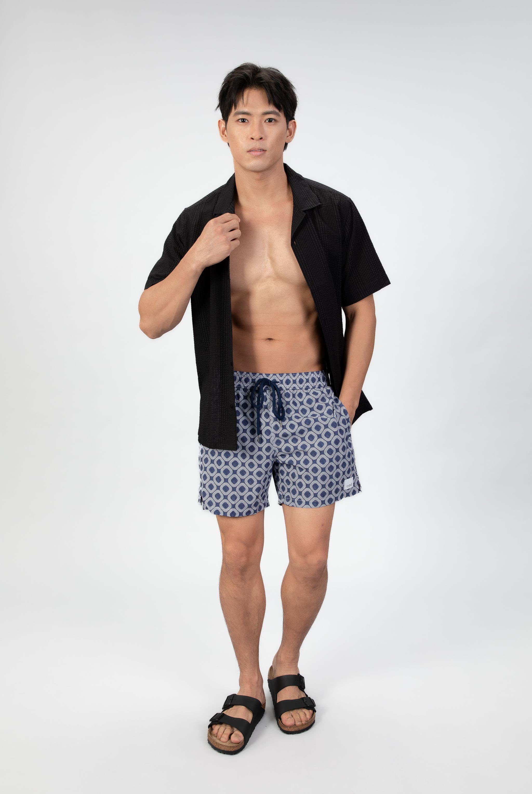 Man wearing blue patterned shorts in navy blue seersucker fabric with a black shirt on a plain background
