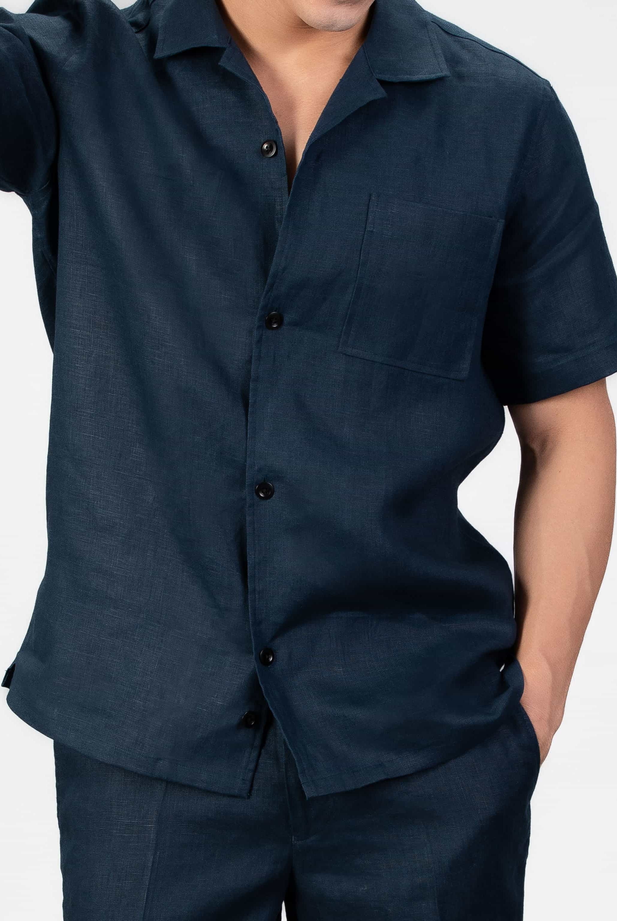 Person wearing navy blue linen set, camp collar shirt and shorts on light gray background