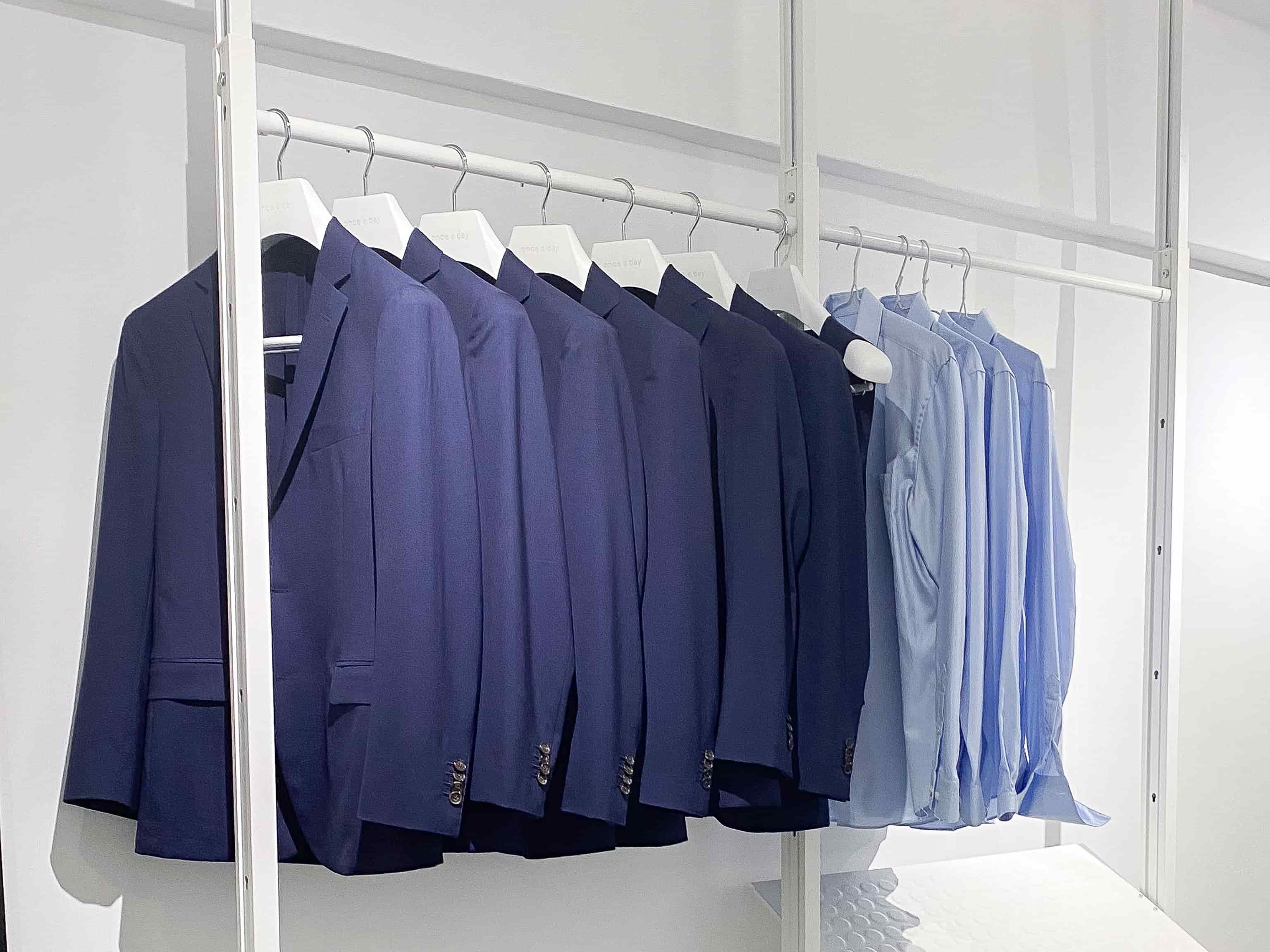 Row of blue suits and light blue shirts on hangers against a white background