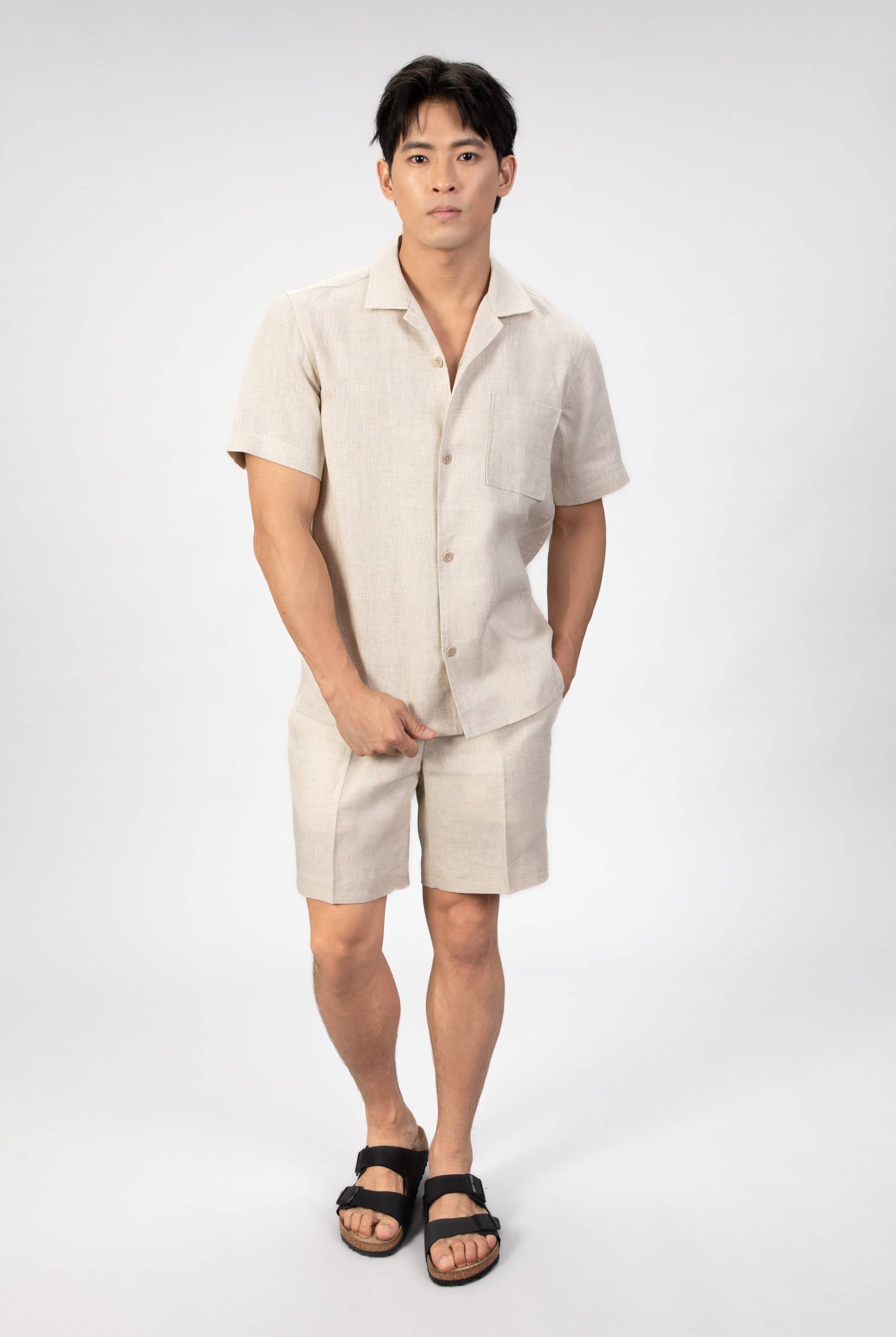 Man wearing a beige linen camp collar shirt and shorts set on a light gray background