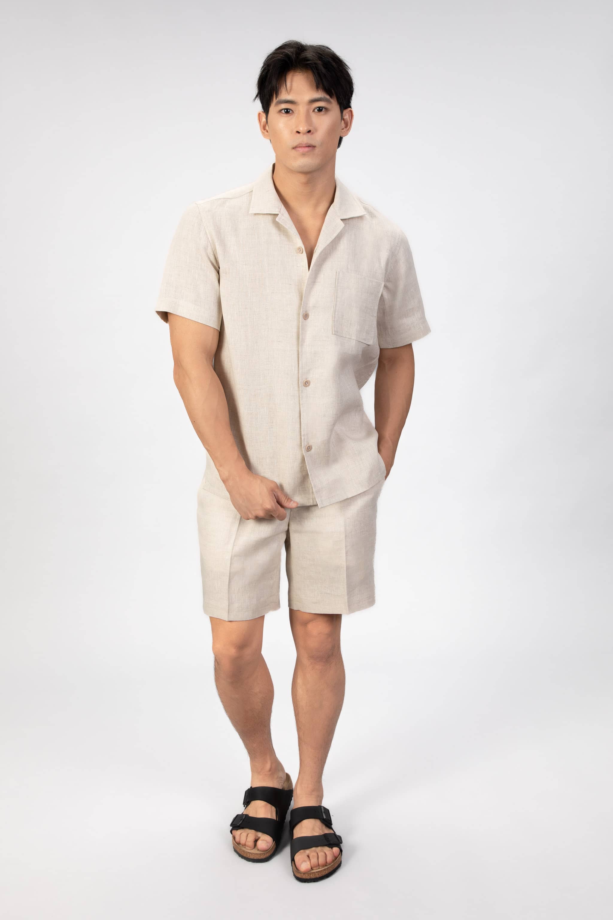 Man wearing a beige linen camp collar shirt and shorts set on a light gray background