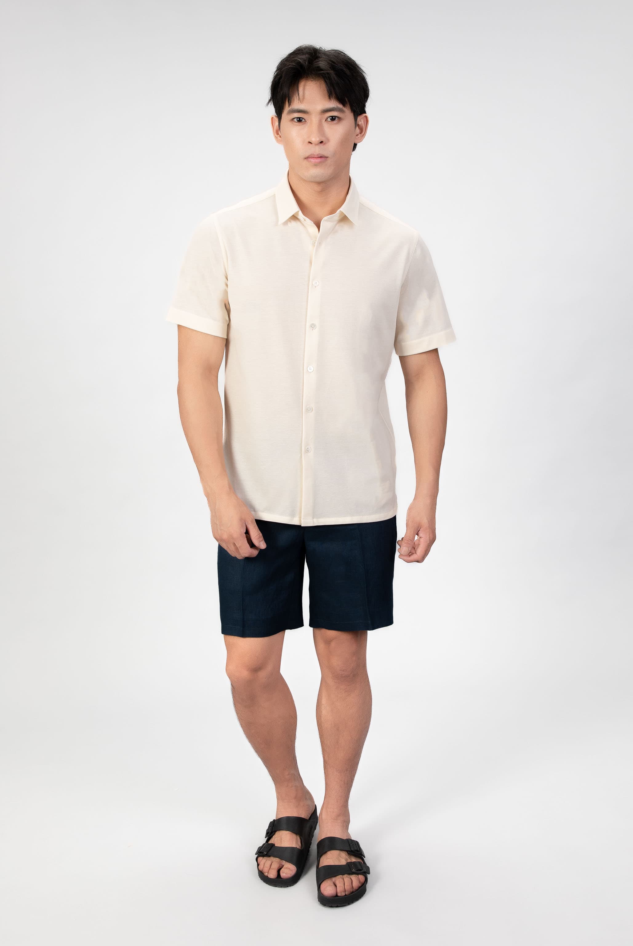 Man wearing a sand-beige piquet polo shirt sleeve shirt with linen navy shorts on a light gray background