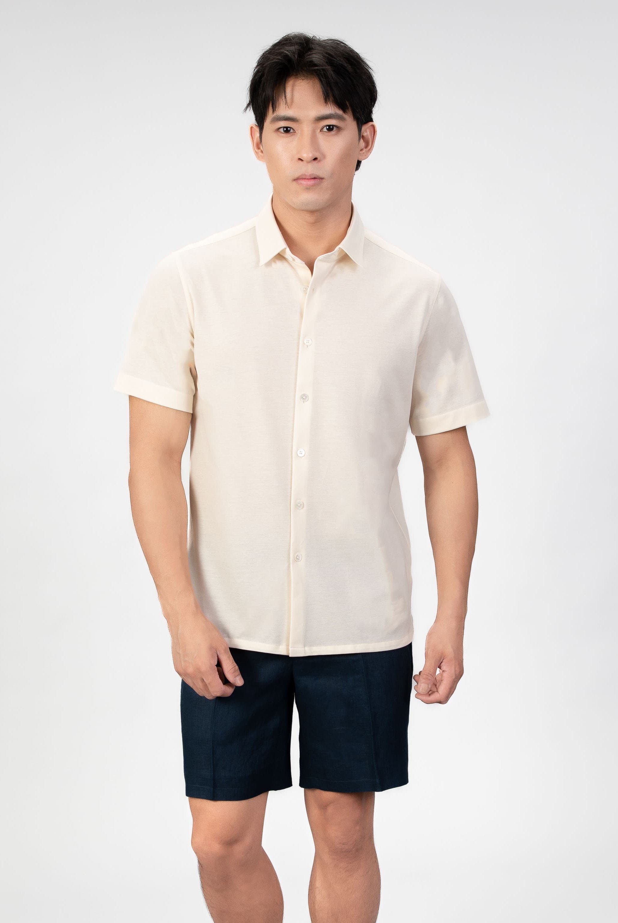 Man wearing a sand-beige piquet polo shirt sleeve shirt with linen navy shorts on a light gray background