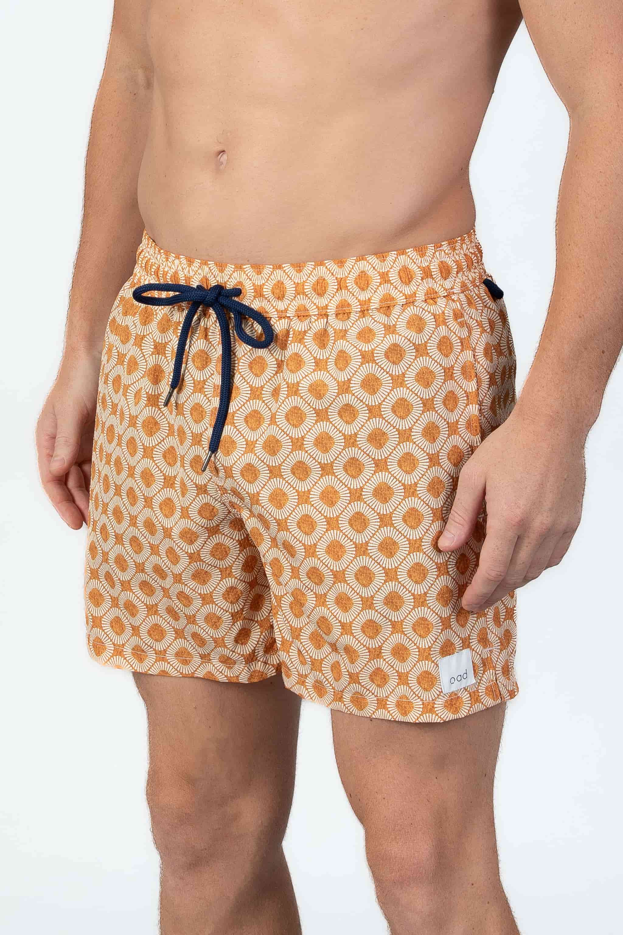 Model wearing orange patterned swim shorts with a navy drawstring on a white background