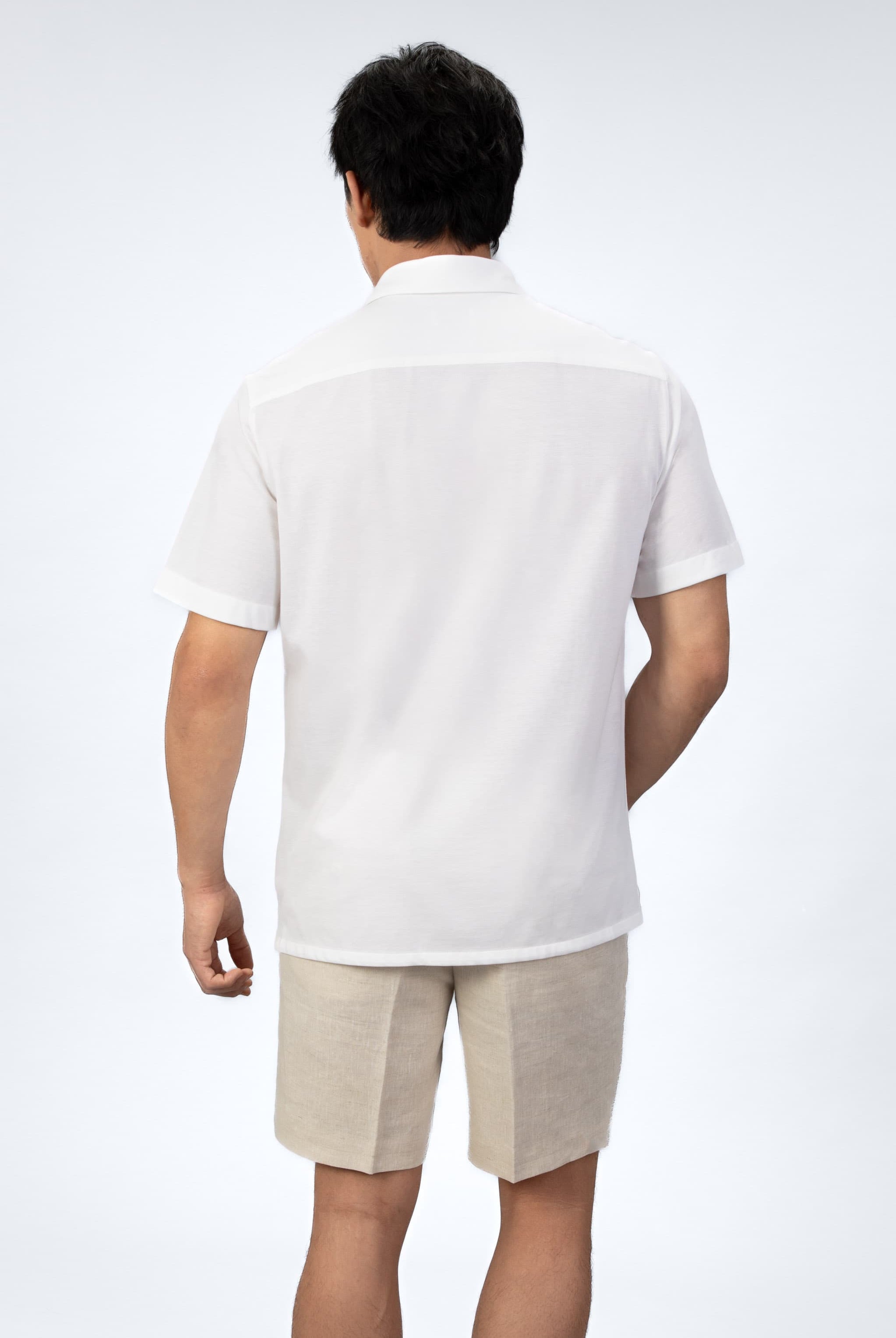 Man wearing a white short-sleeve shirt and beige shorts on a light gray background