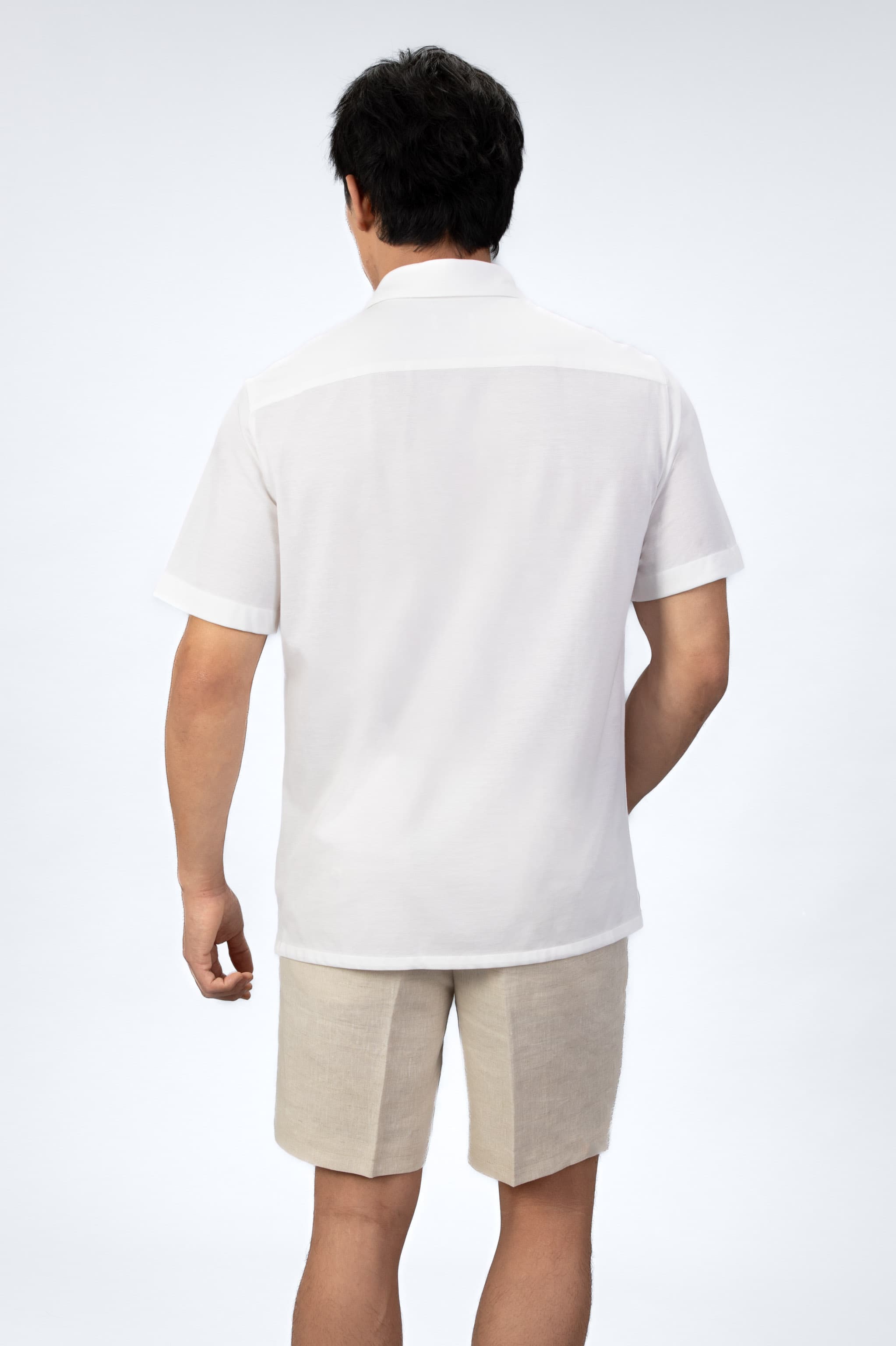 Man wearing a white short-sleeve shirt and beige shorts on a light gray background