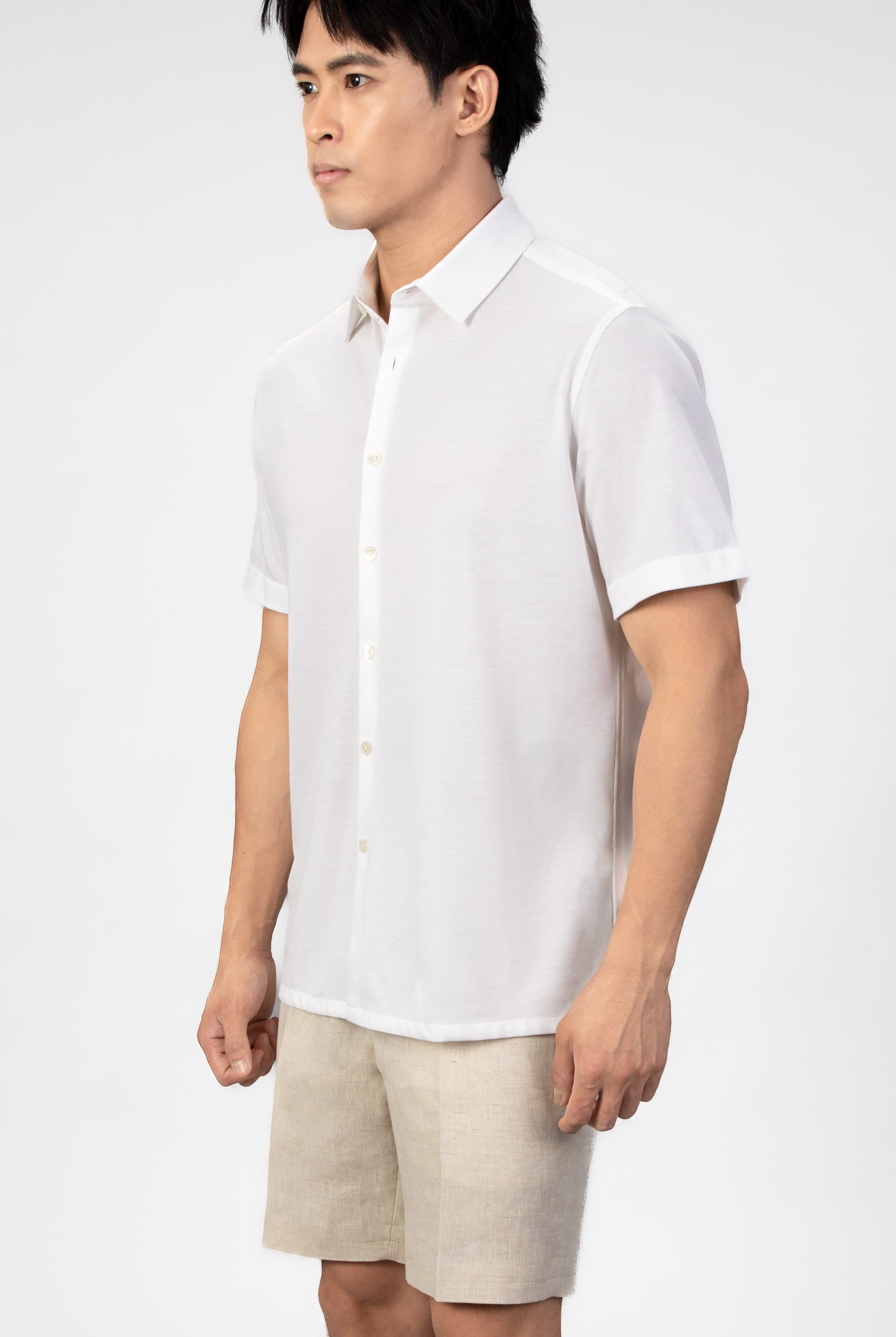 Man wearing a white short-sleeve shirt and beige shorts on a plain background