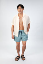 Comfortable, soft aqua blue lounge swim shorts shown from the front, with an elastic waistband paired with a seersucker camp collar shirt in light sand color. 