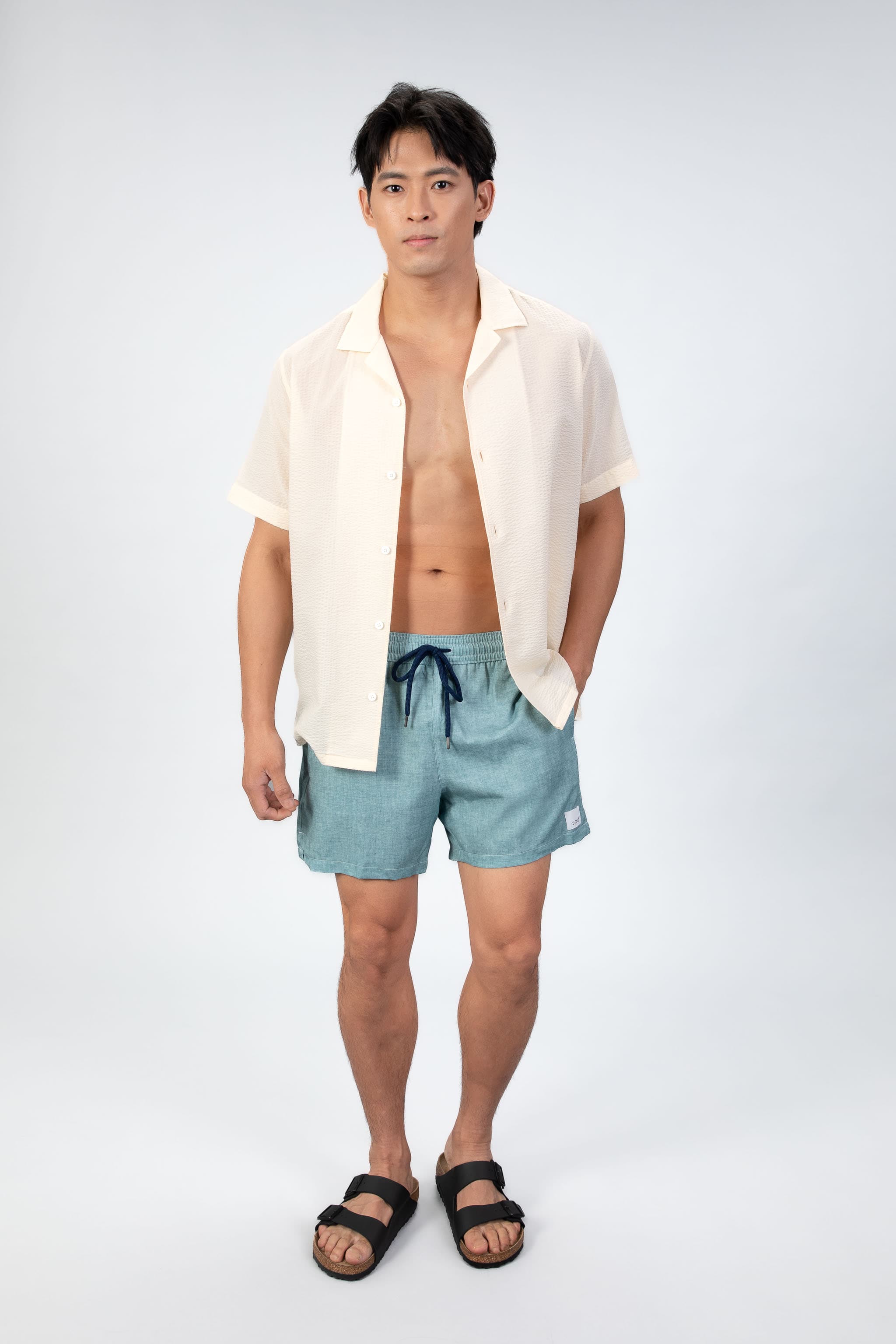 Comfortable, soft aqua blue lounge swim shorts shown from the front, with an elastic waistband paired with a seersucker camp collar shirt in light sand color. 