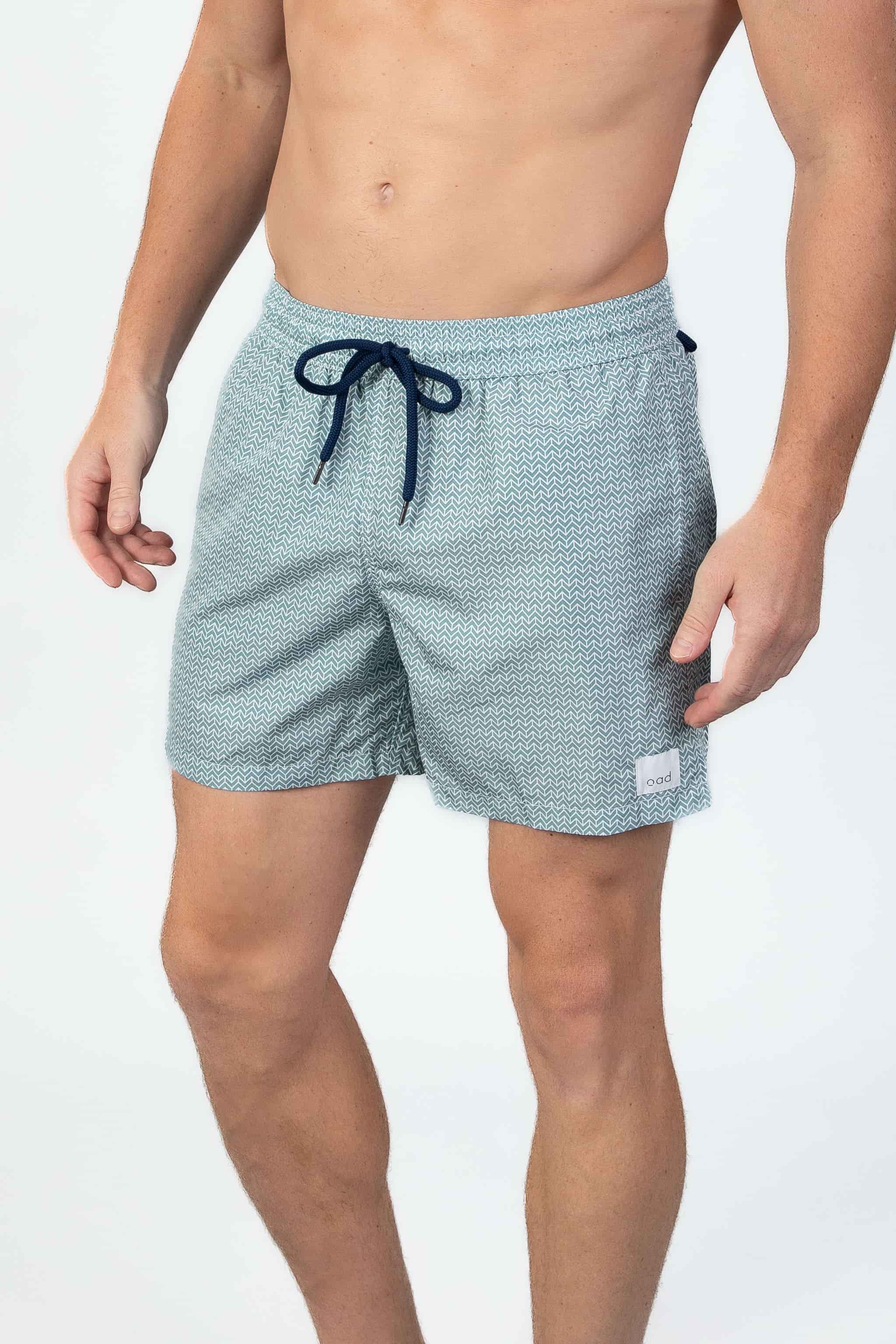 Person wearing patterned swim shorts in Aqua turquoise with a navy drawstring on a light gray background