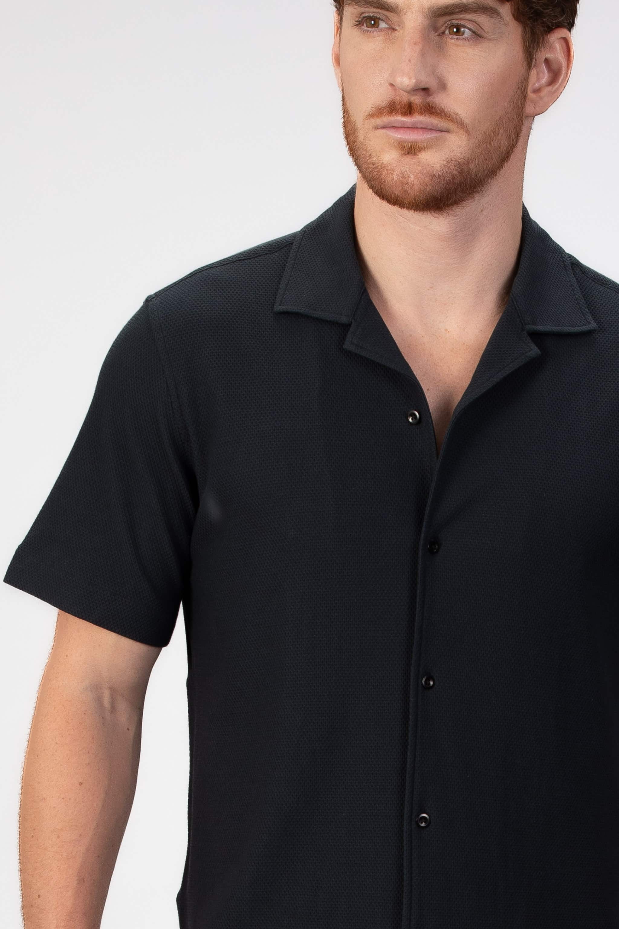 Man wearing a black short-sleeve camp collar shirt on a plain background
